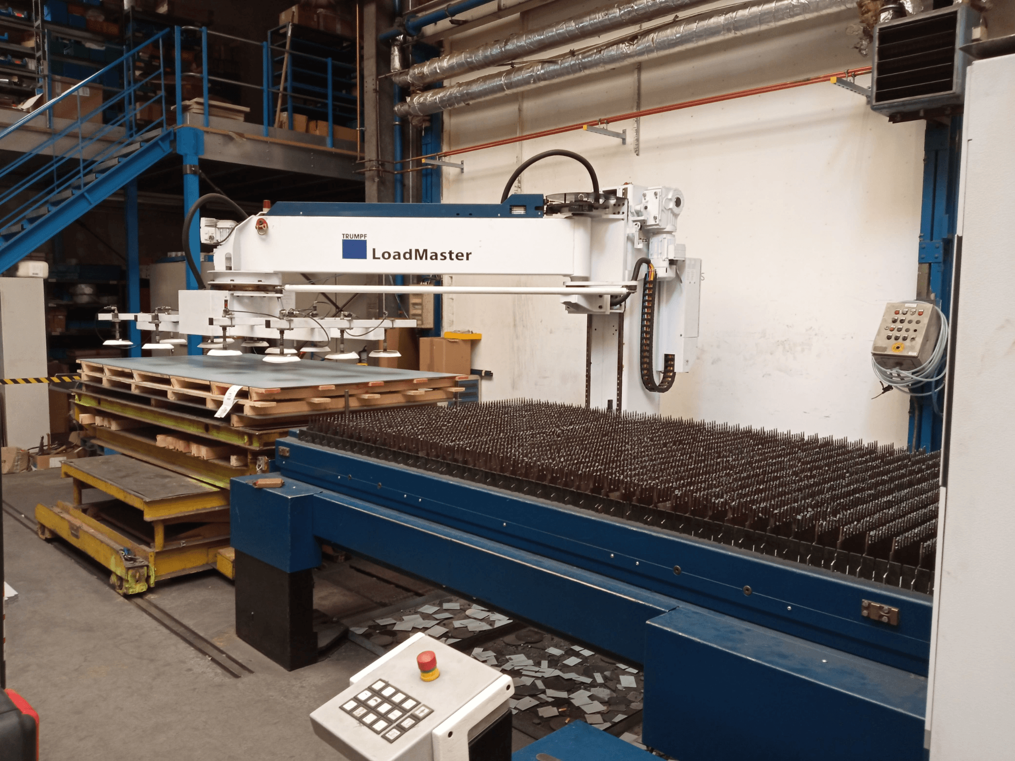 TRUMPF TruLaser 3030 CO₂ lāzergriešanas iekārta no sāniem, kurā redzams LoadMaster un materiālu paletes.