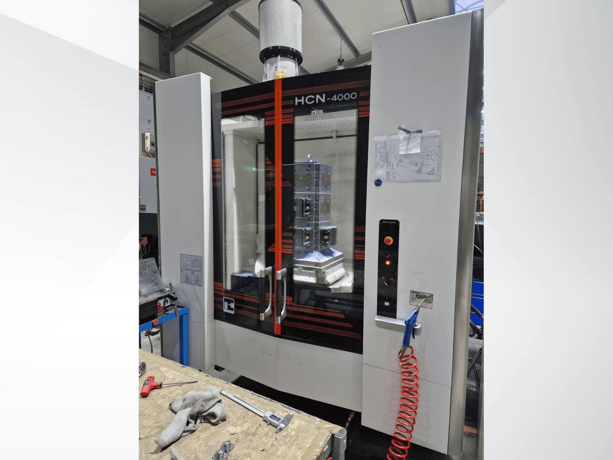 HCN-4000 CNC darbgalds priekšpusē ar stikla paneli, vadības paneli ar pogām un pievienotu rasējumu.
