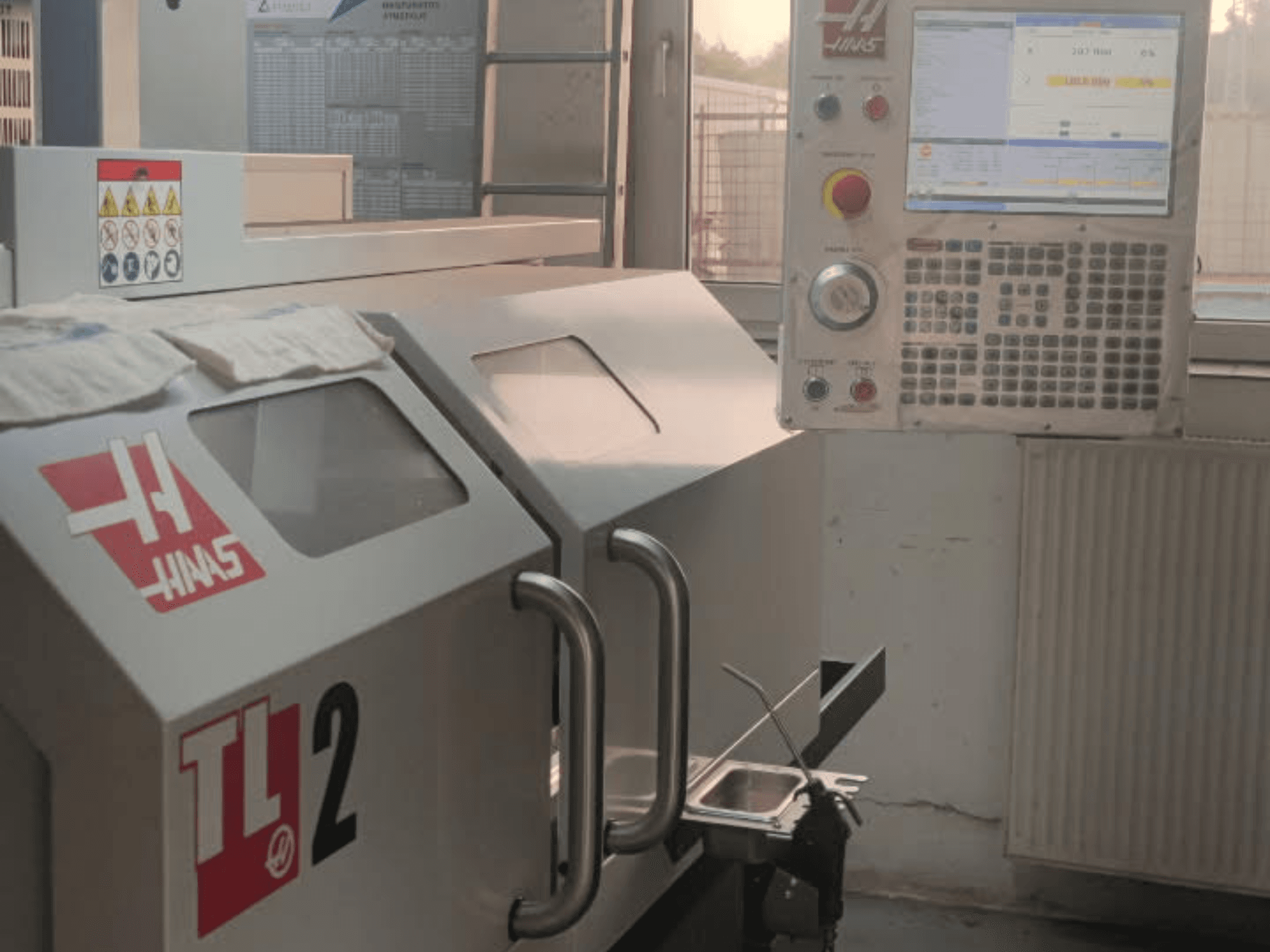 Haas TL-2 horizontālās virpošanas mašīnas priekšējais skats ar vadības paneli, metāla korpusu un drošības zīmēm.