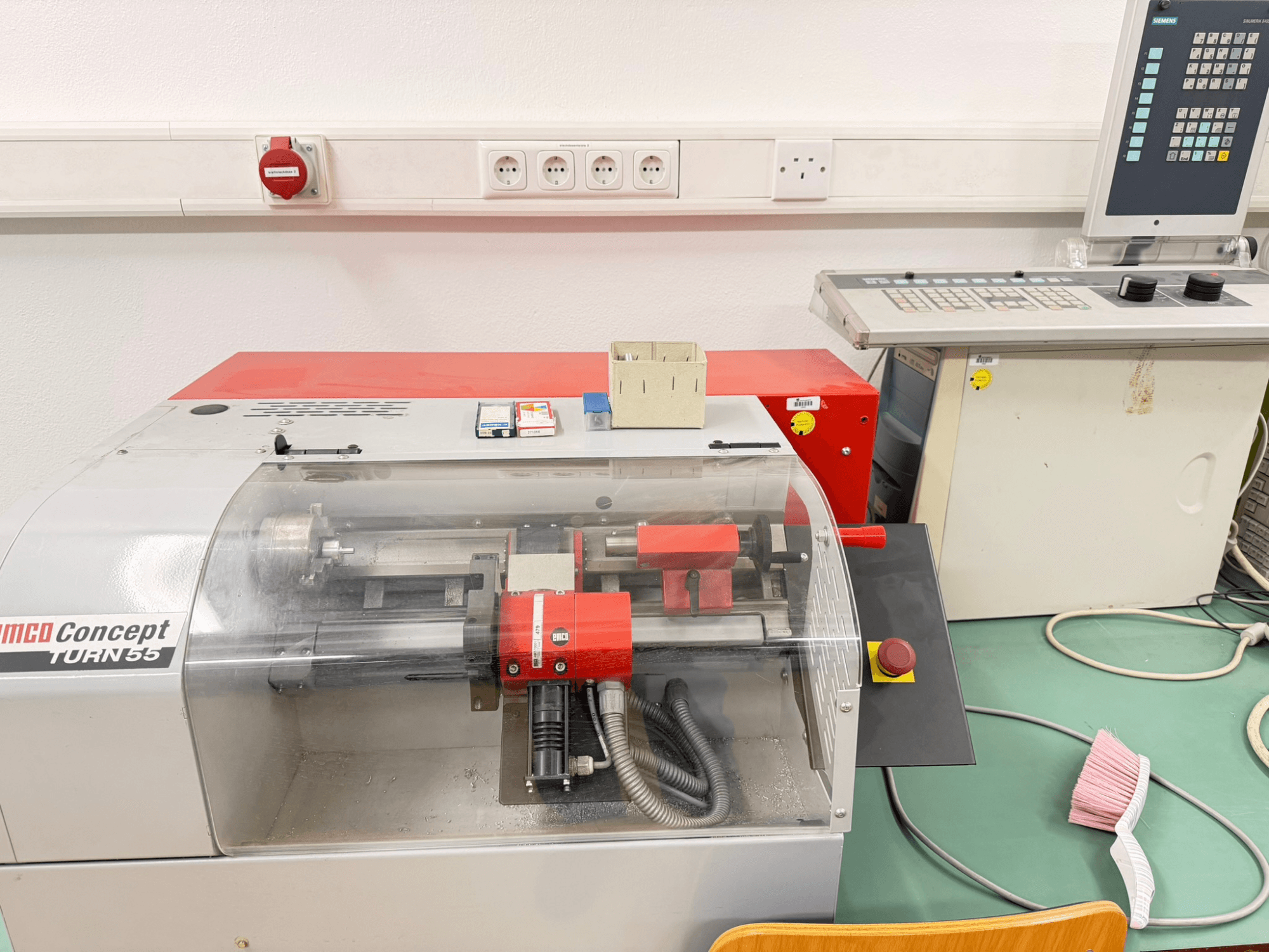 EMCO Concept Turn 55 horizontālās virpošanas iekārta ar sarkanu un pelēku ārējo apdari, priekšējais skats, kurā redzamas vadības ierīces un darba zona.