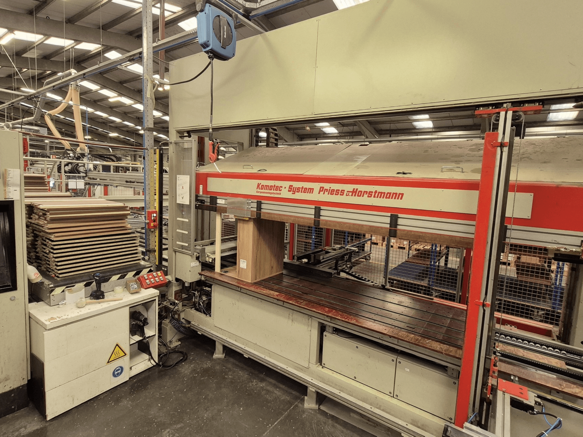 PREISS U HORTSTMANN finiera prese KP-5-CNC, priekšējais skats, kurā redzamas sakrautas finiera loksnes un vadības panelis.
