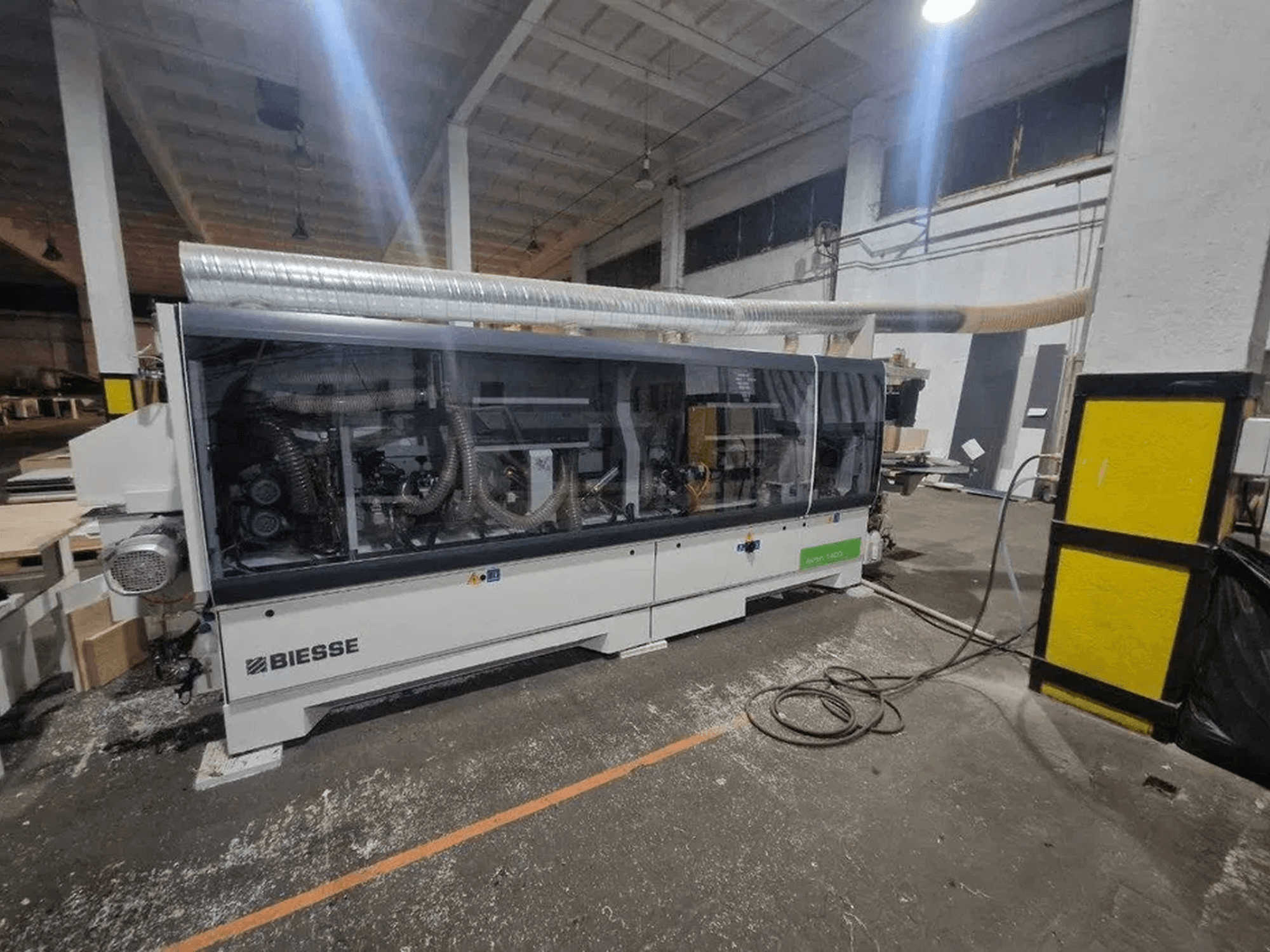 BIESSE Akron 1440 A malu līmēšanas iekārta darbnīcā ar caurspīdīgu apvalku un redzamām iekārtas detaļām.