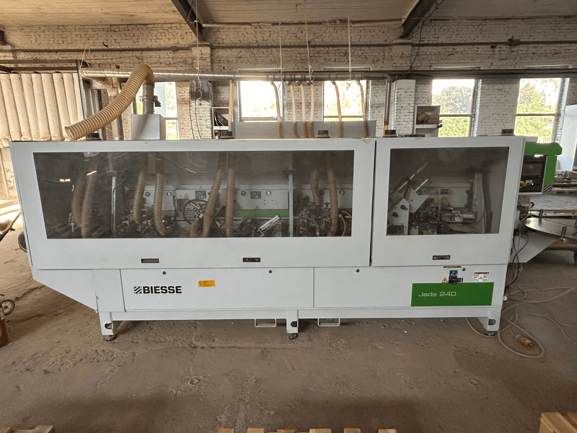 BIESSE Jade 240 malu līmēšanas mašīna baltā un zaļā krāsā, skats no priekšpuses, kurā redzams vadības panelis un mašīnas iekšējā uzbūve.
