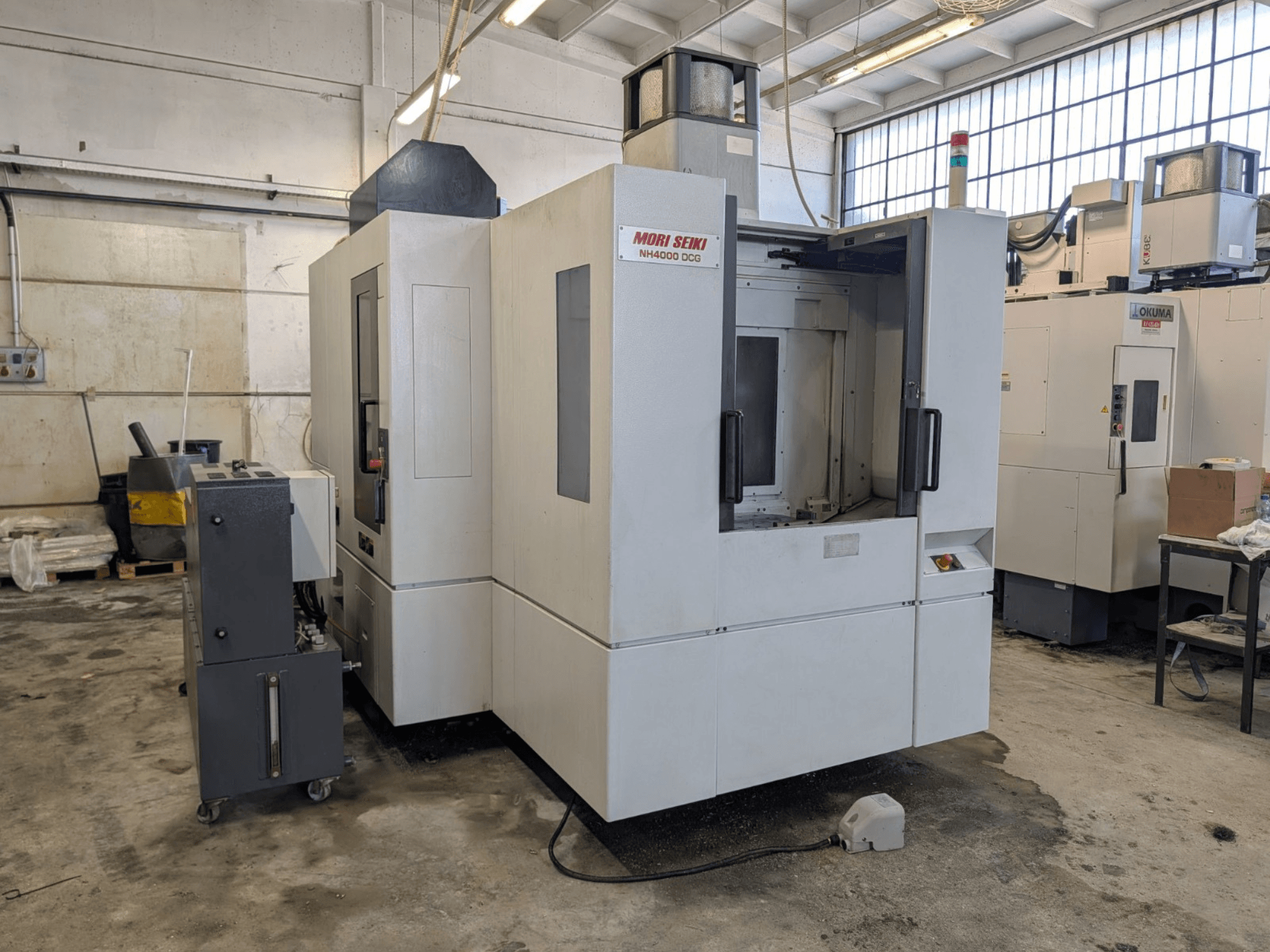 MORI SEIKI NH 4000 DCG horizontālais apstrādes centrs, skats no priekšpuses, redzams vadības panelis un darba zona, pelēka un balta apdare.