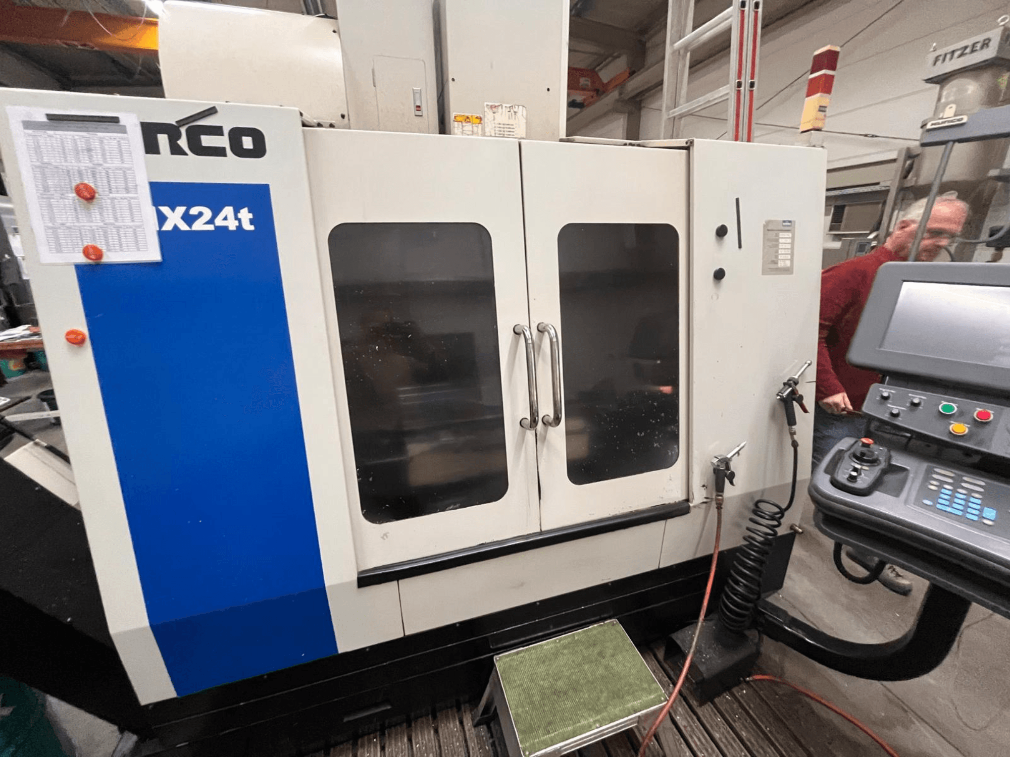 Hurco vertikālais apstrādes centrs, modelis VX24t, parādīts no priekšpuses ar vadības paneli un caurspīdīgām durvīm.