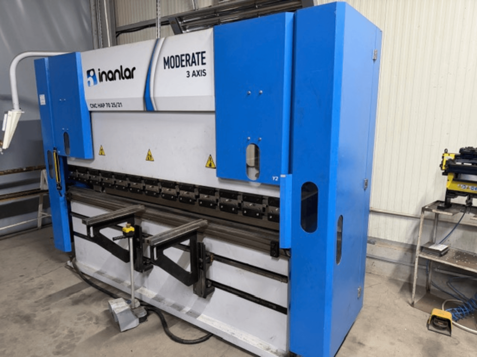 Inanlar Moderate 3 asu CNC darbgalds zilā krāsā, skats no priekšpuses, uz korpusa redzamas vadības sviras un drošības marķējumi.