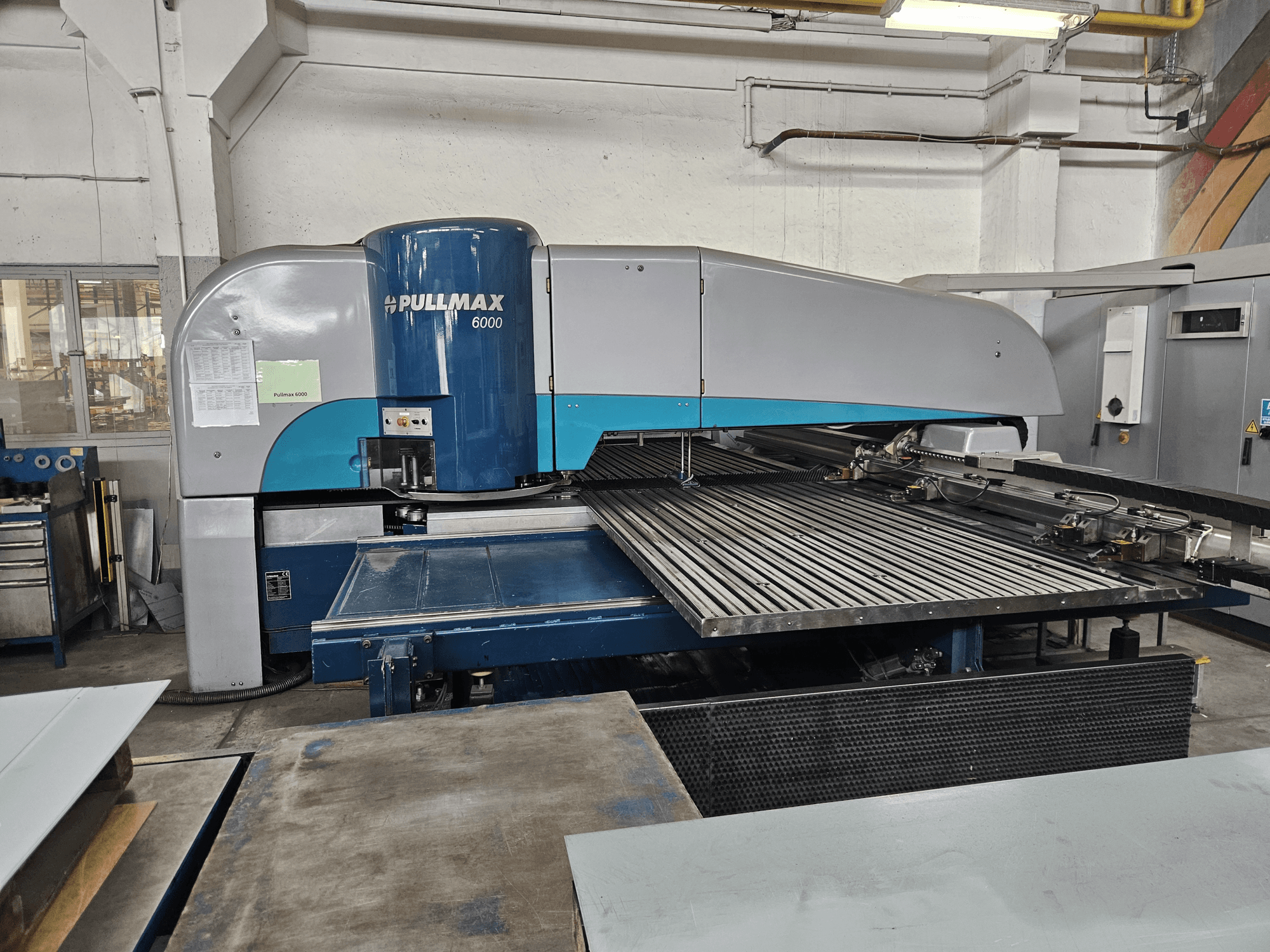 Pullmax 6000 CNC caurumošanas mašīnas priekšējais skats, kurā redzams tās lielais plakanais paliktnis un metāla karkass darbnīcā.