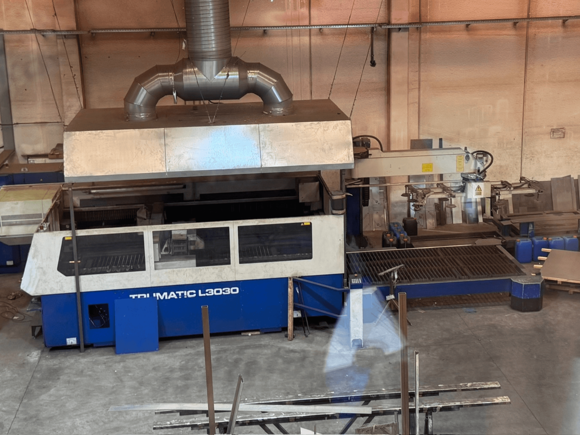 CO₂ lāzergriešanas iekārta TRUMPF TRUMATIC L3030 darbnīcā, skats no priekšpuses, kurā redzams vadības panelis un griešanas galds.