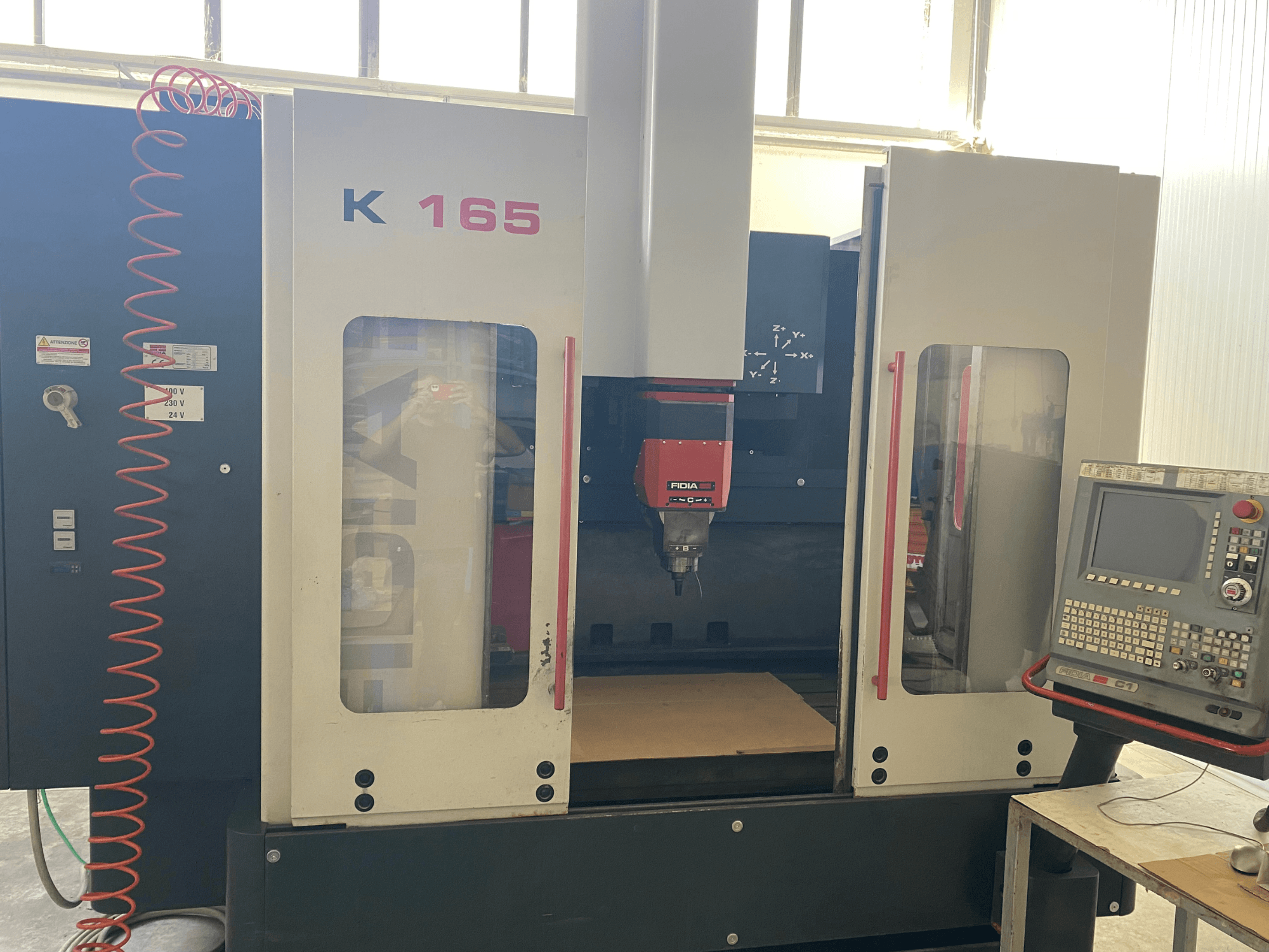 Fidia K 165 CNC darbagalds ar sarkanu vārpstu un vadības paneli, skatīts no priekšpuses, labi apgaismotā darbnīcā.