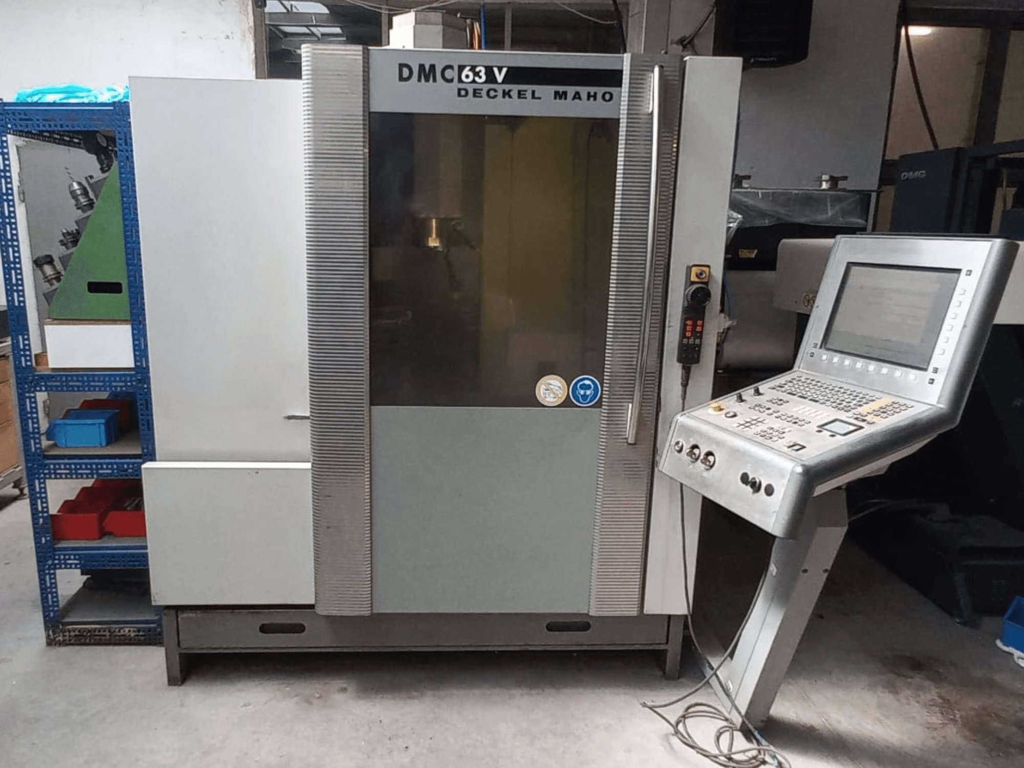 DMG DECKEL MAHO DMC 63V vertikālā apstrādes centra skats no priekšpuses ar vadības paneli un redzamu darba zonu.