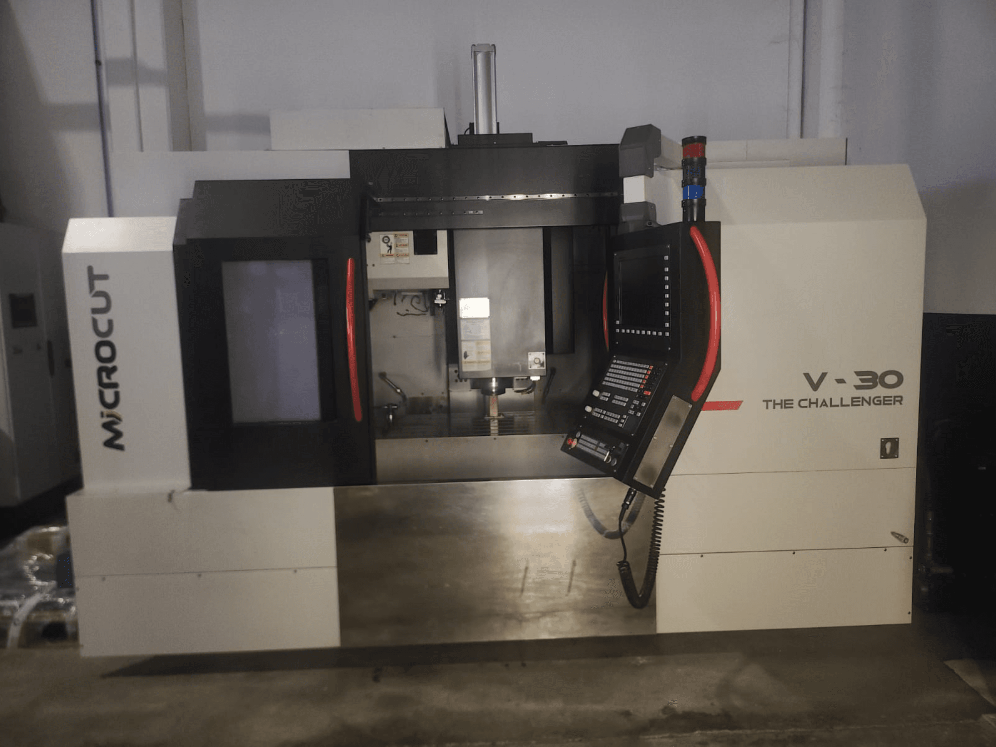 Microcut V-30 Challenger CNC mašīna, skats no priekšpuses, ar vadības paneli, griešanas zonu un industriālā dizaina elementiem.