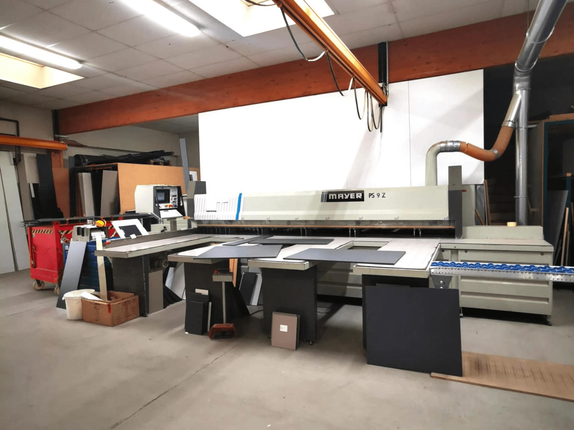 MAYER PS9 Z griešanas iekārta darbnīcā, skats no priekšpuses, redzami dažādi materiāli un konveijera sistēma.