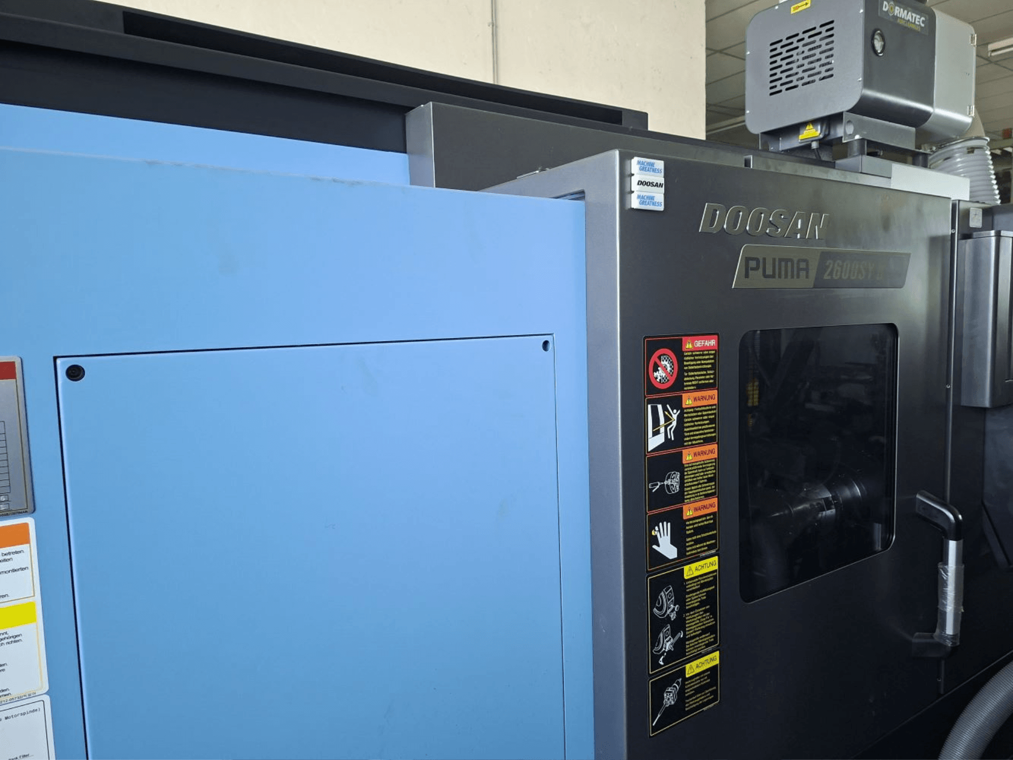 DOOSAN PUMA 2600 SY II horizontālās virpošanas iekārta, skats no priekšpuses, ar drošības marķējumu un zilu paneli.