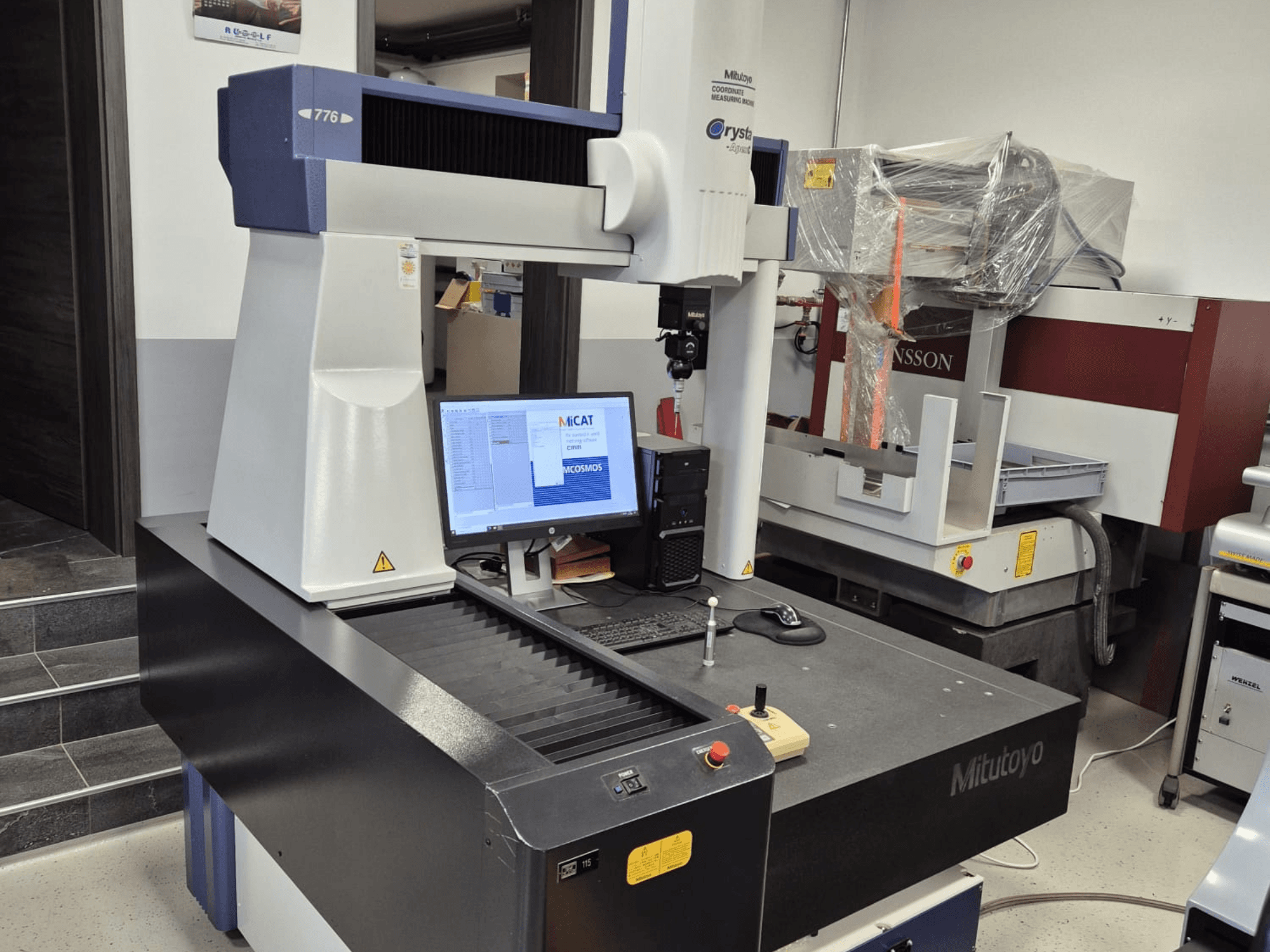 Mitutoyo 776 modeļa 776 koordinātu mērīšanas iekārta priekšpusē, ar redzamu monitoru, uz kura redzama mērīšanas programmatūra un vadības ierīces.