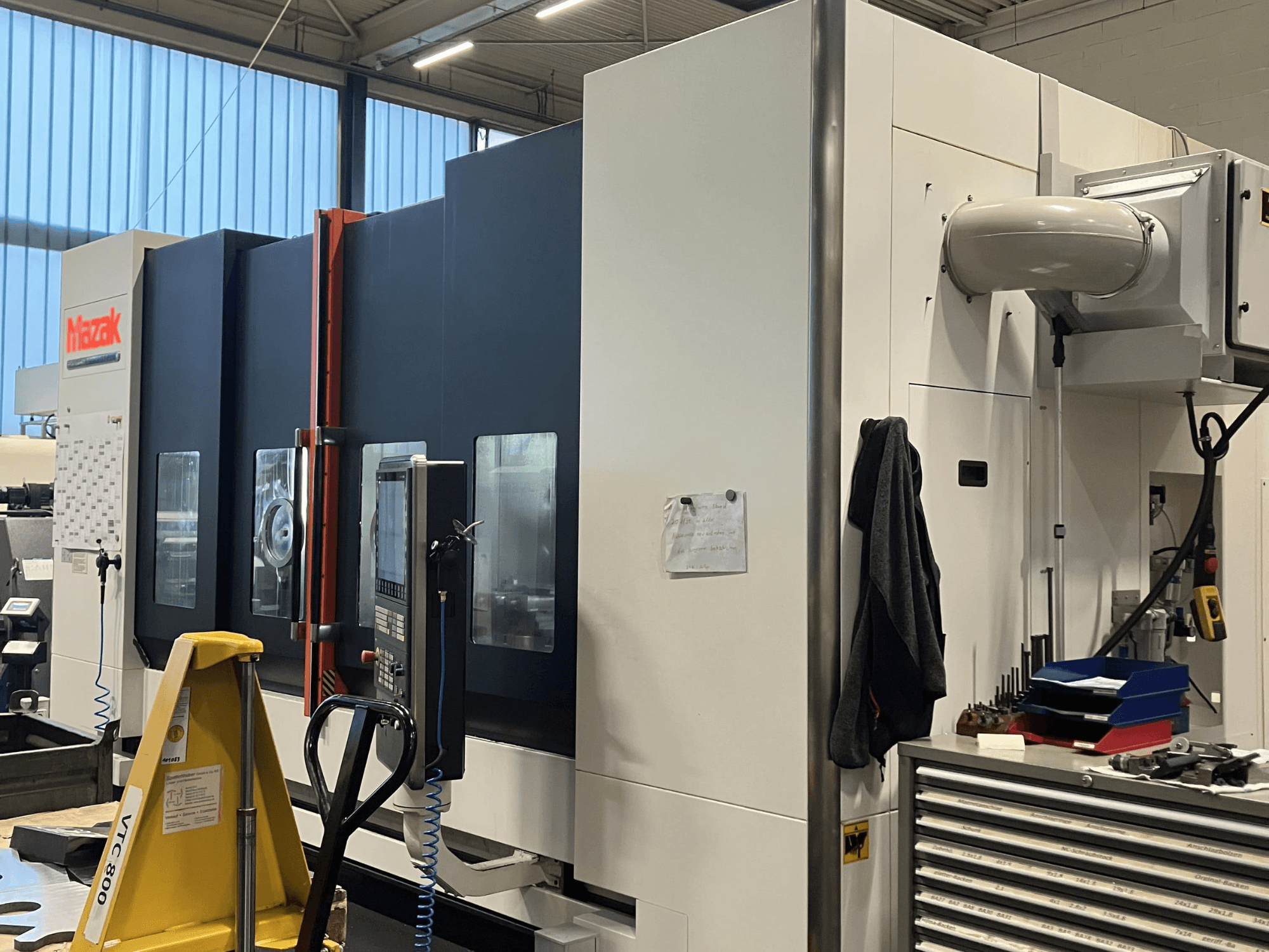 Mazak CNC darbagalds no sāniem, kurā redzams vadības panelis un drošības elementi darbnīcā.