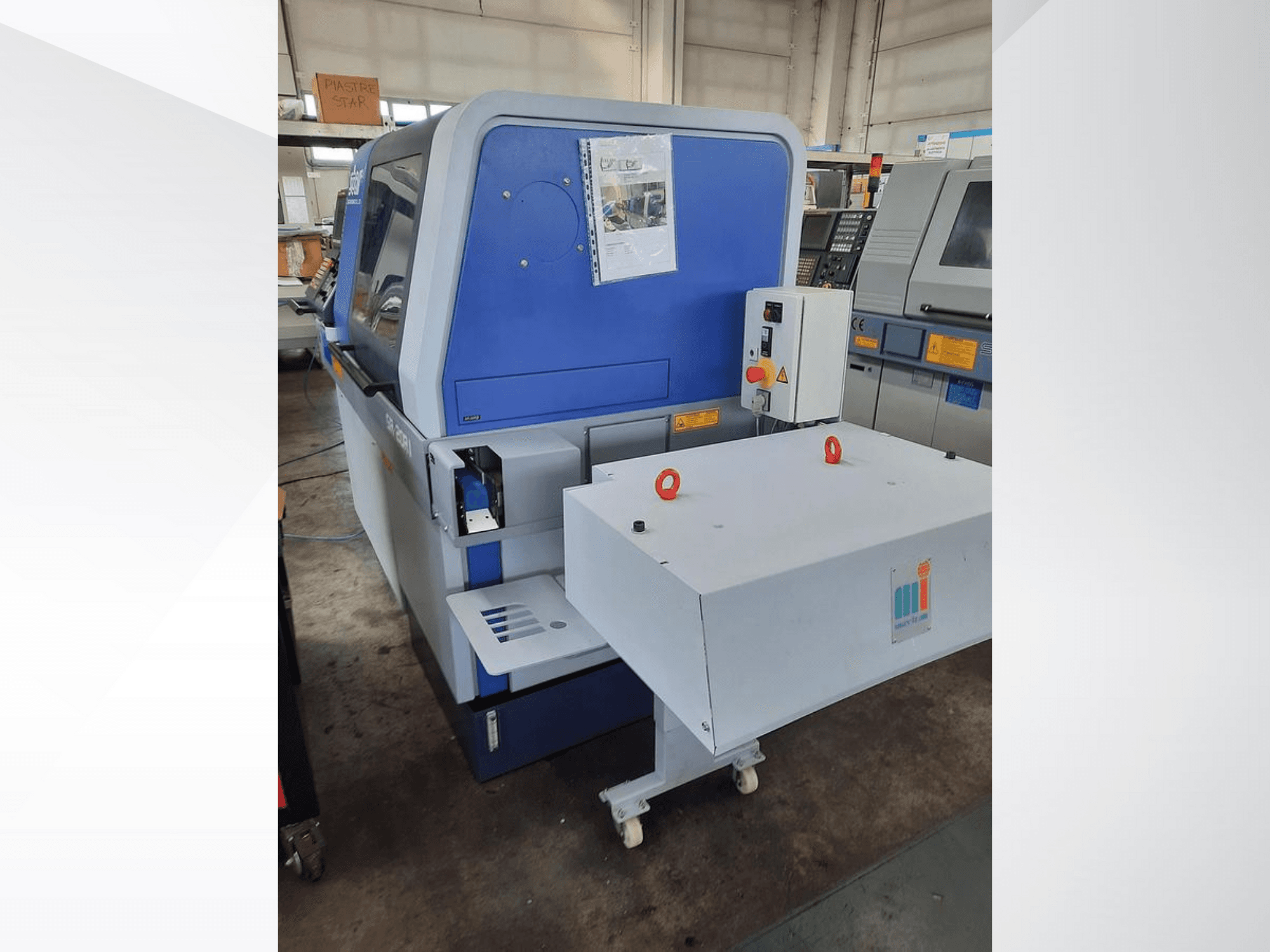 Zila rūpniecības mašīna ar baltu konveijeru, ar vadības paneli un pievienotajiem drošības elementiem, skats no sāniem.