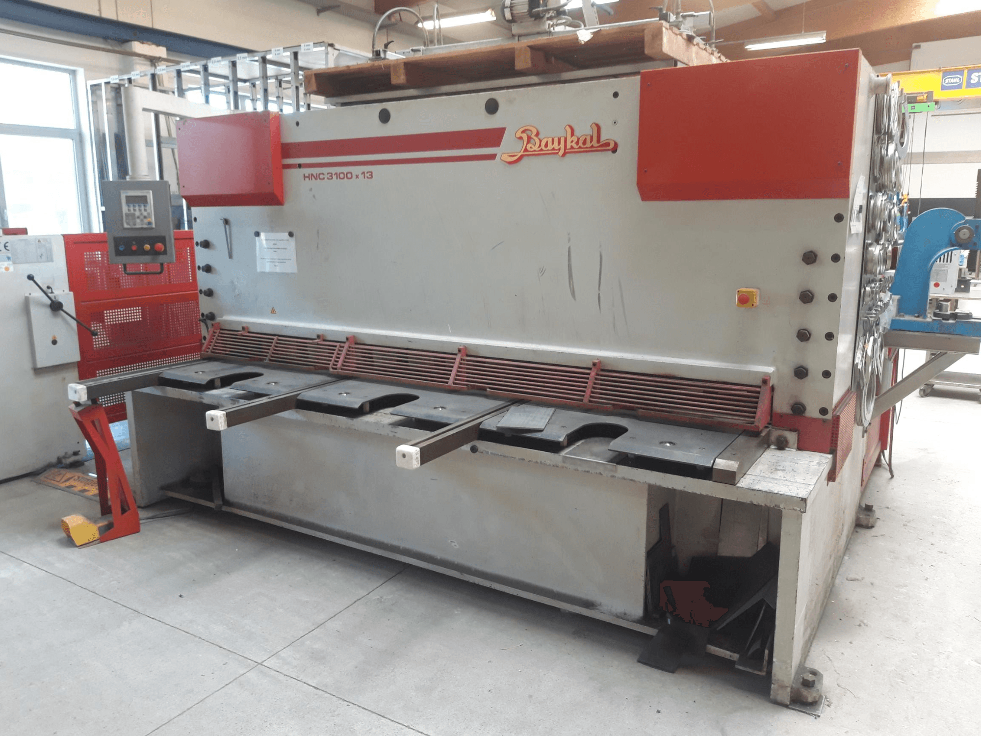 Baykal HNC 3100x13 CNC griešanas stenda skats no priekšpuses, kurā redzams vadības panelis, metāla griešanas zona un atkritumu savākšanas telpa.