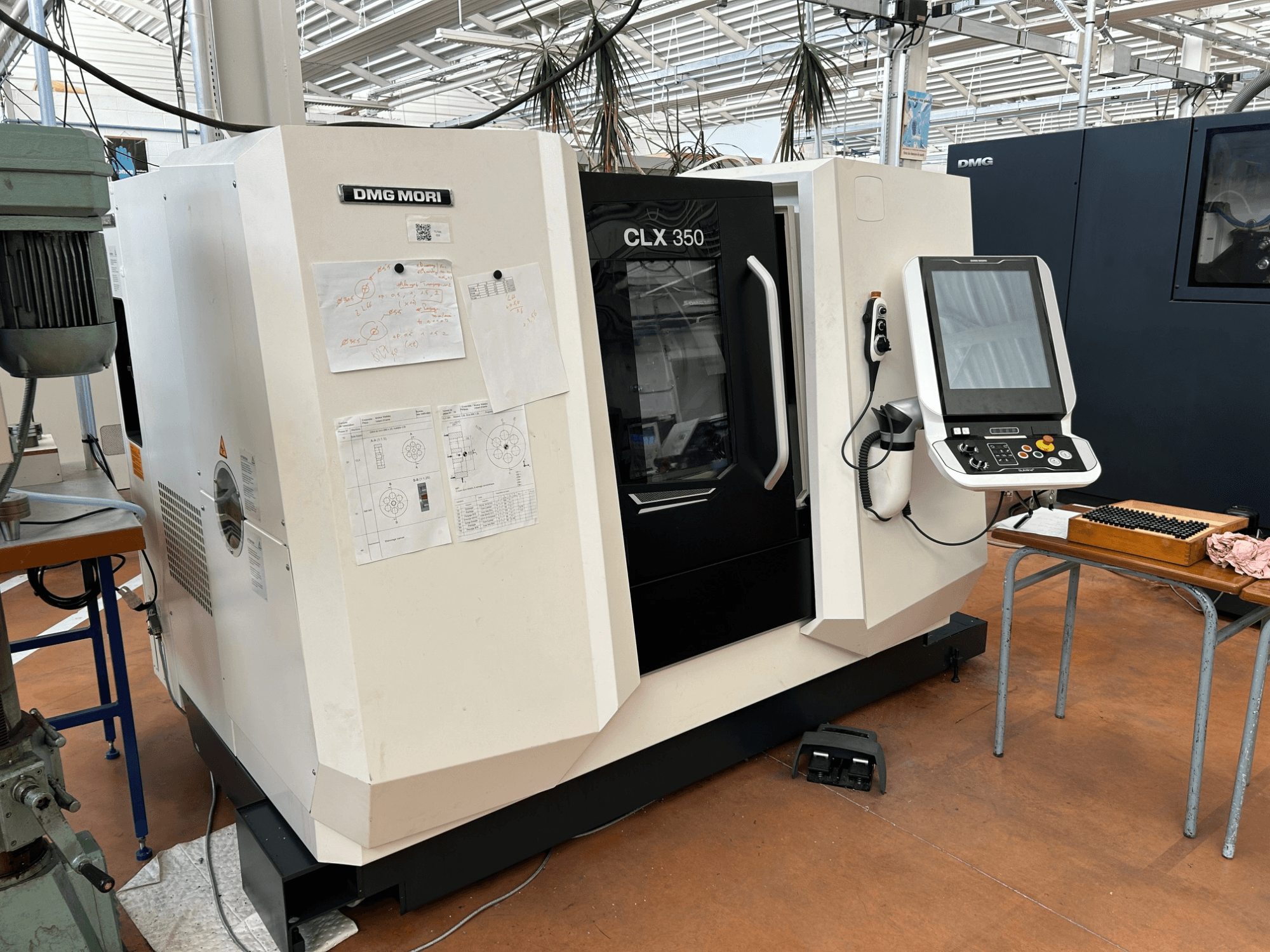 DMG MORI CLX 350 V4 horizontālā virpošanas mašīna, skats no priekšpuses ar vadības paneli un pievienotajiem tehniskajiem dokumentiem.