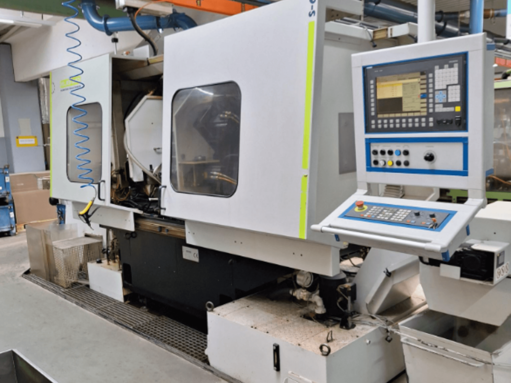 Rūpnieciskā frēzmašīna ar vadības paneli, skats no sāniem, ar divām kamerām un redzamiem cauruļvadu savienojumiem.