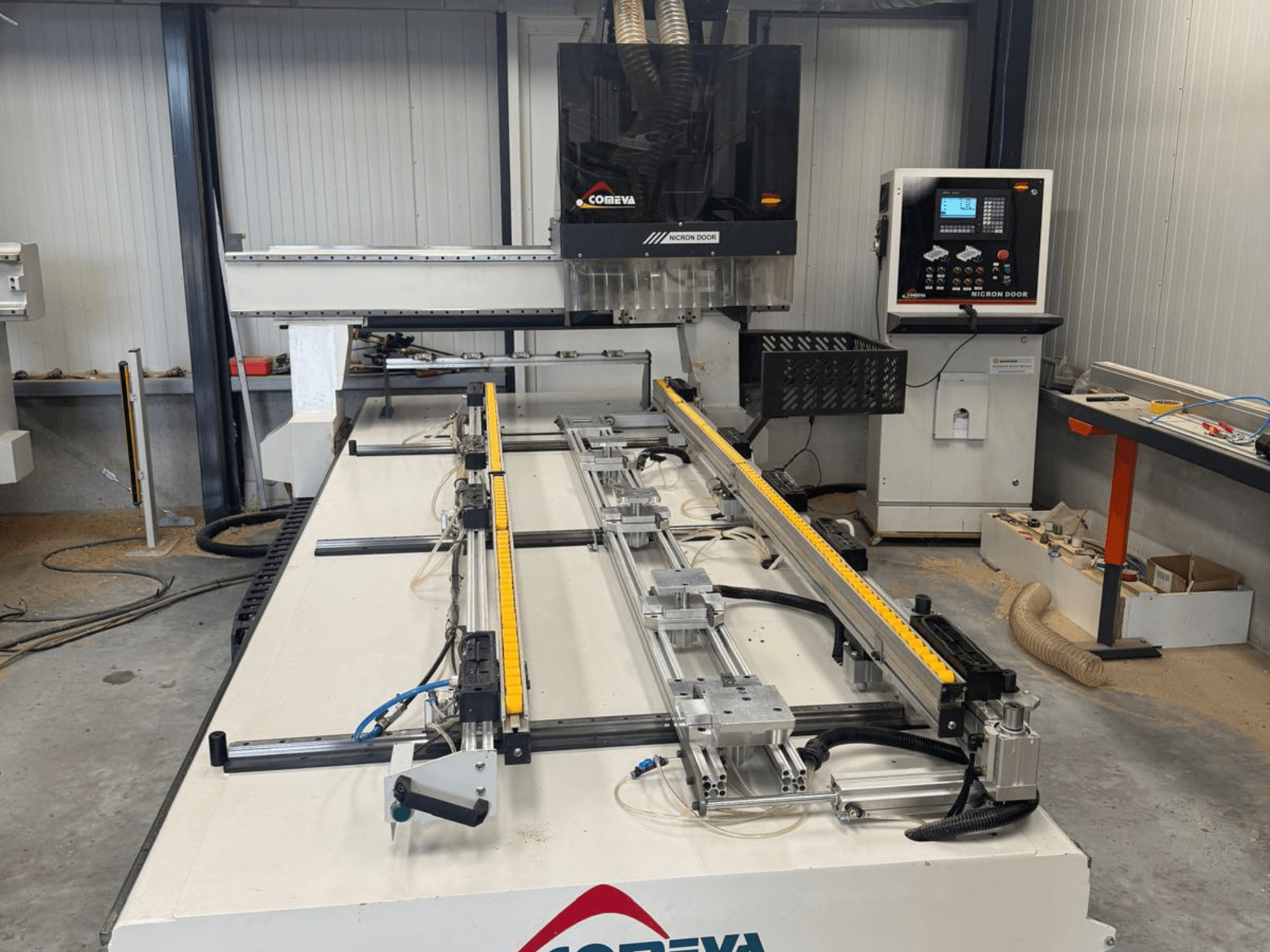 CNC koka apstrādes centrs COMEVA MEX V 2100x3260, skats no priekšpuses, kurā redzama darba stacija, vadības panelis un vadības sliedes.