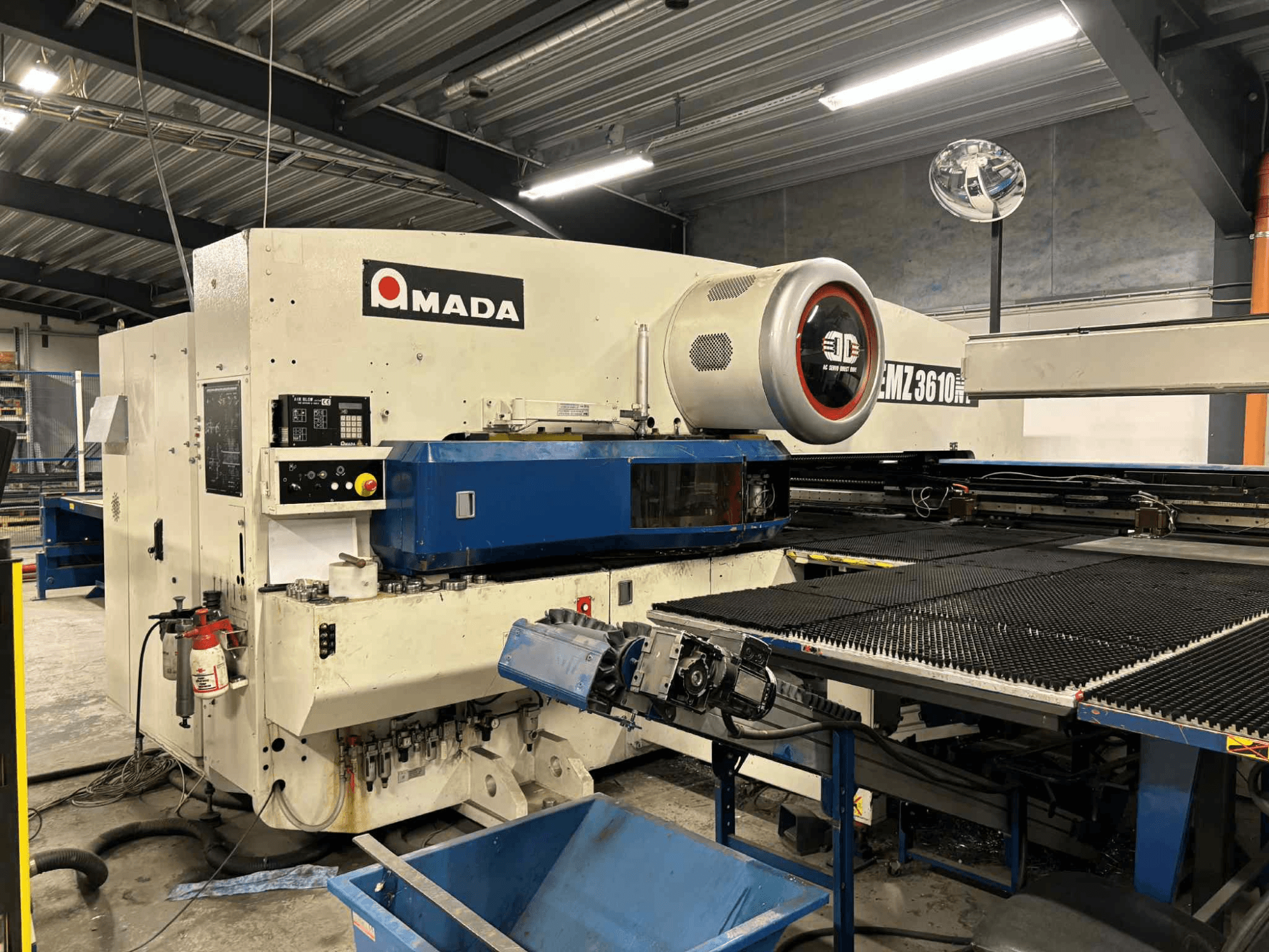 Amada EMZ3610H perforators, skatīts no priekšpuses; darbības vadības elementi, zilā gultne un drošības aprīkojums.