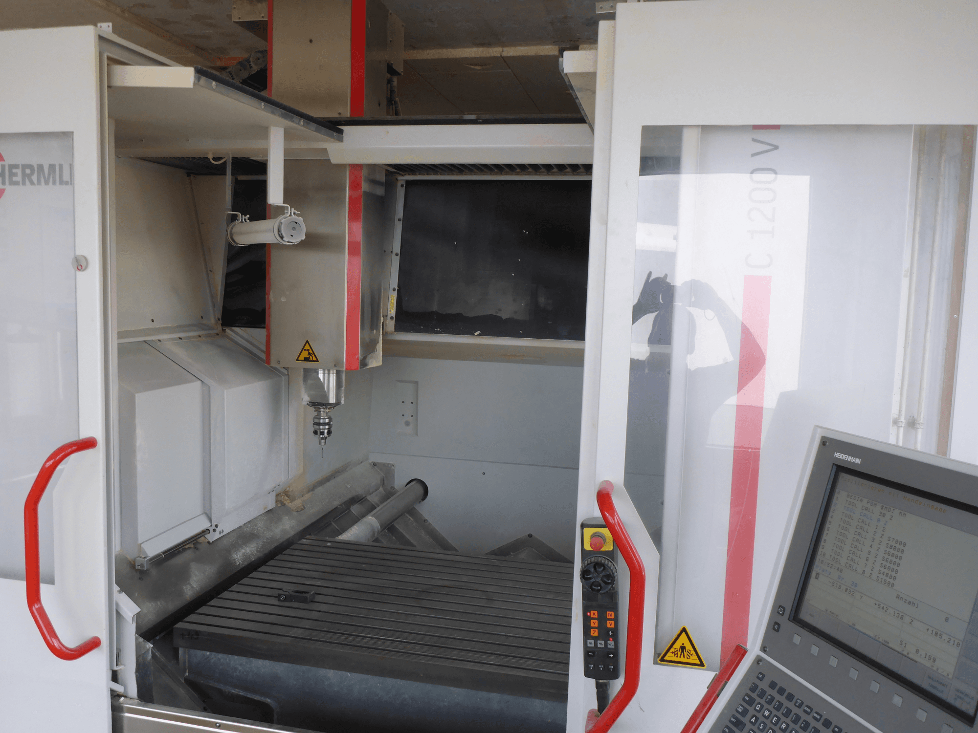 HERMLE C 1200 vertikālā apstrādes centra interjers, kurā redzams instrumentu turētājs, vadības panelis un darba galds no priekšpuses.