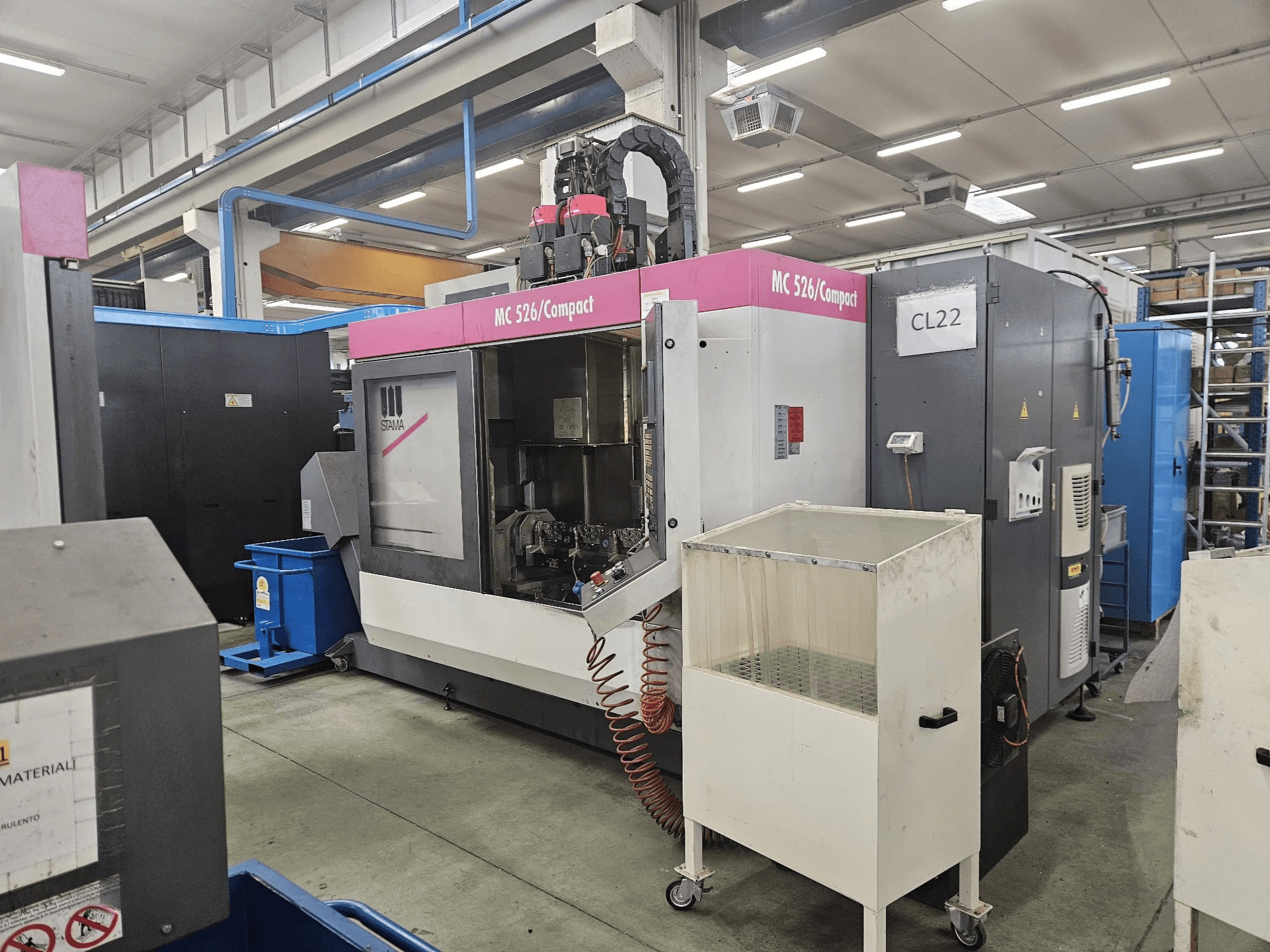 MC 526 kompakta CNC mašīna no Stama, sānu skats, kurā redzams vadības panelis, dzesēšanas šķidruma tvertne un blakus esošās iekārtas.