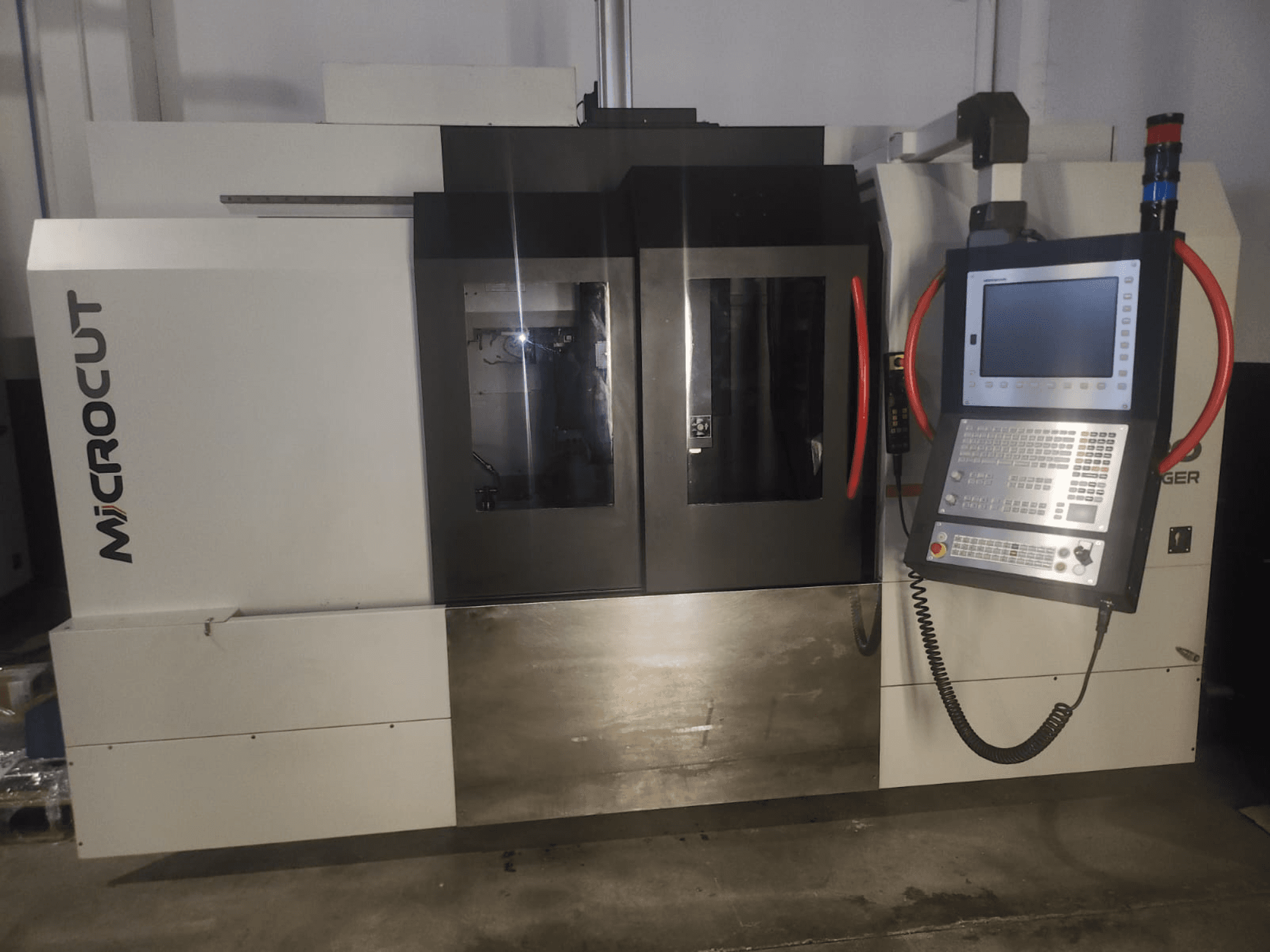 Microcut CNC mašīna, skatoties no priekšpuses; vadības panelis, divi logi, rūpniecisks dizains un metāliska apdare.