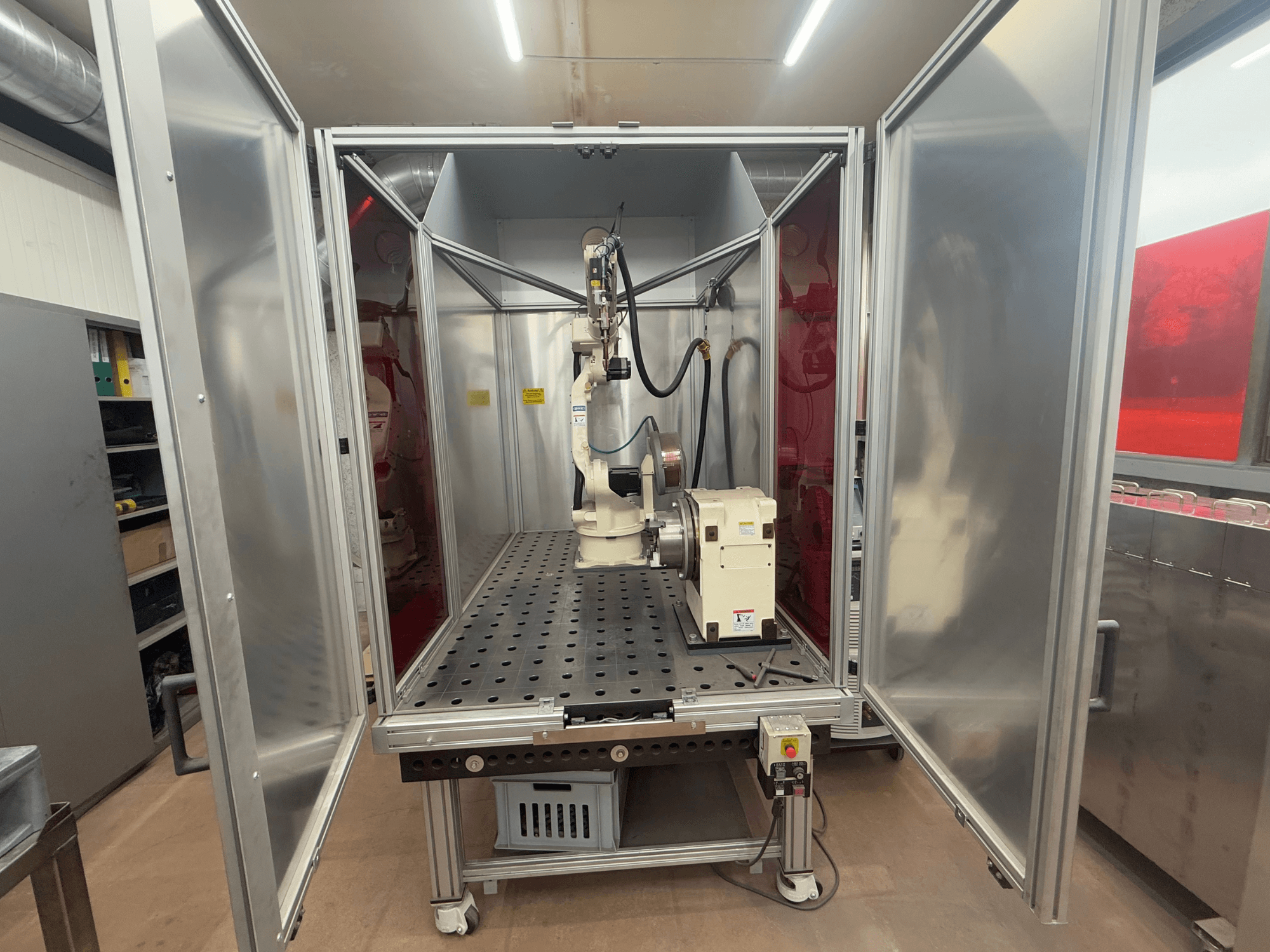 Metināšanas robots OTC Daihen EASY ARC V02.04 metāla korpusā, skatīts no priekšpuses, ar šarnīrveida roku un vadības paneli.