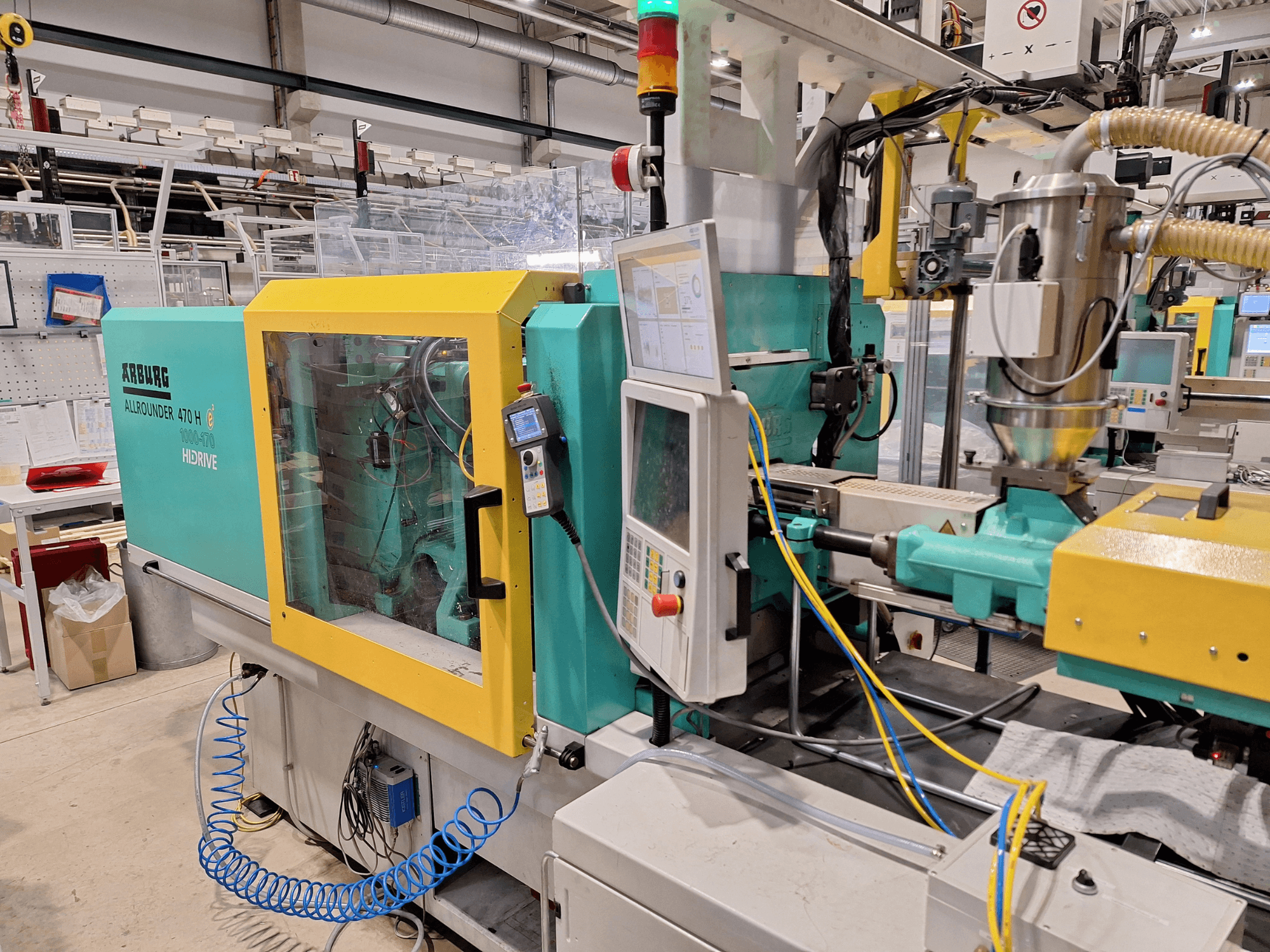 Arburg 470 H 1000-170 hidrauliskā iesmidzināšanas iekārta, sānu skats, kurā redzams vadības panelis un padeves sistēma.