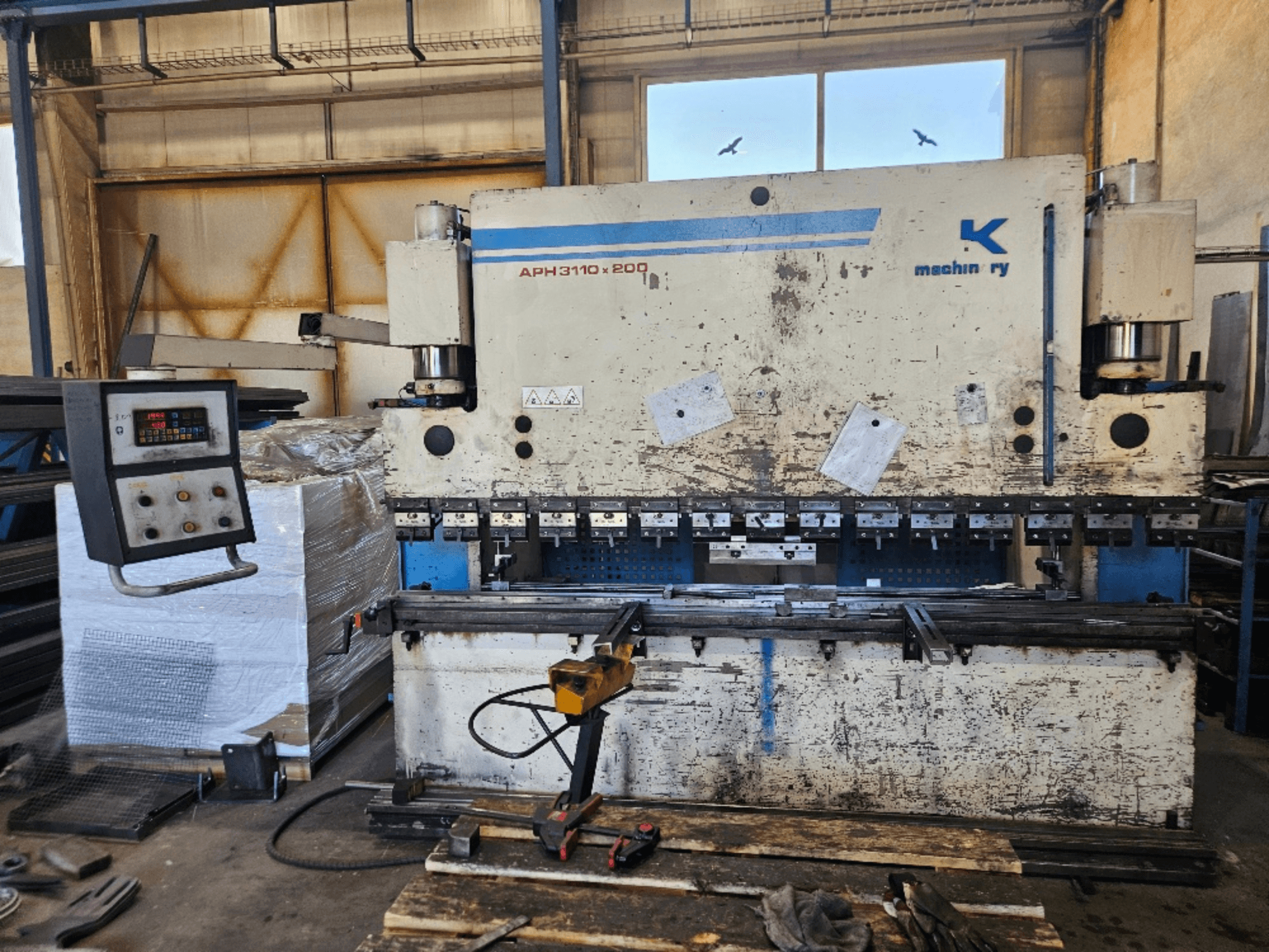 Baykal APH 3110x200 preses bremze darbnīcā, skats no priekšpuses, redzams vadības panelis, metāla loksnes un instrumenti.