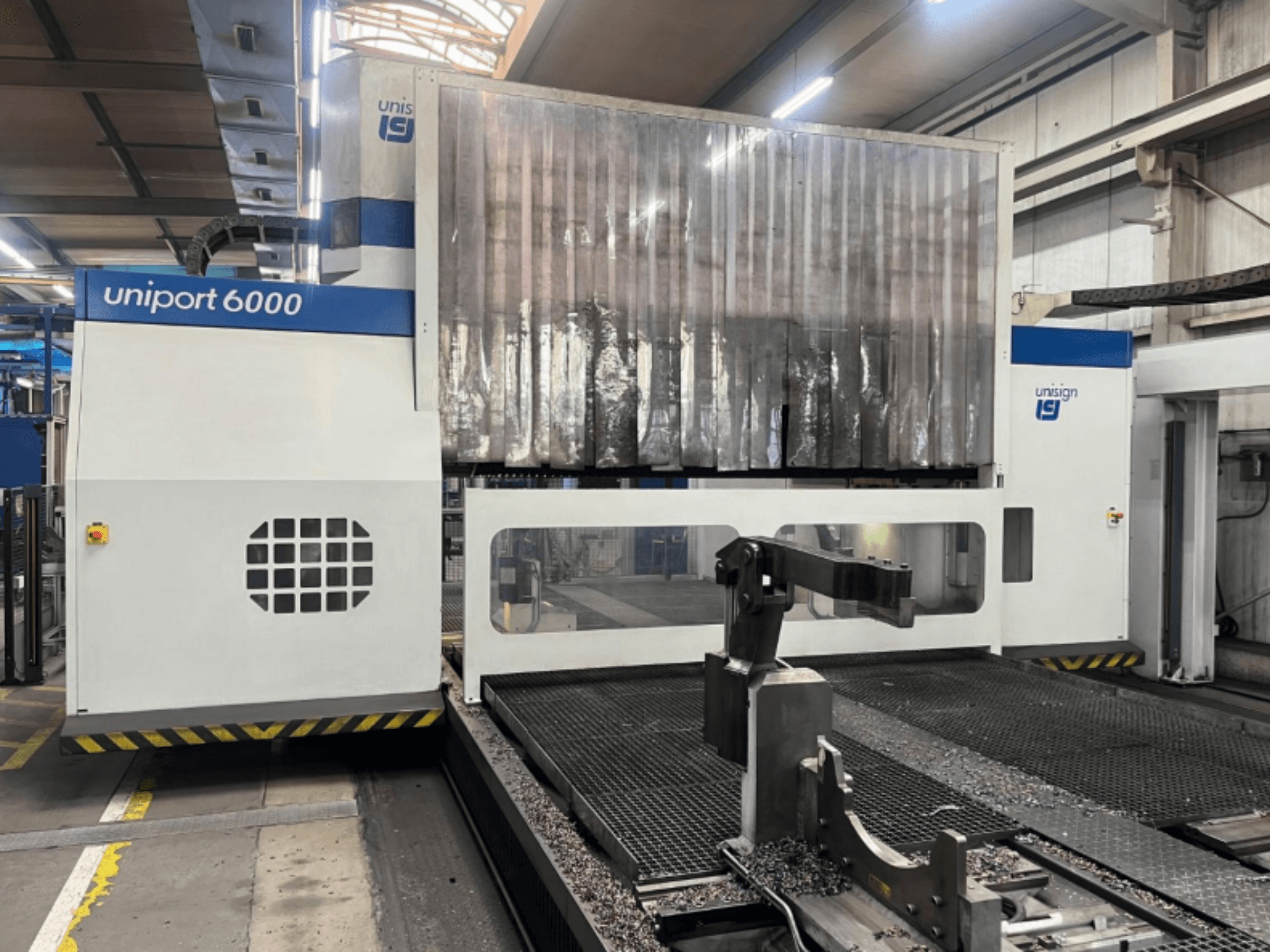 Portālfrēzmašīna Unisign uniport 6000, priekšējais skats, kurā redzama mašīnas konstrukcija un griešanas zona ar metāla skaidām.