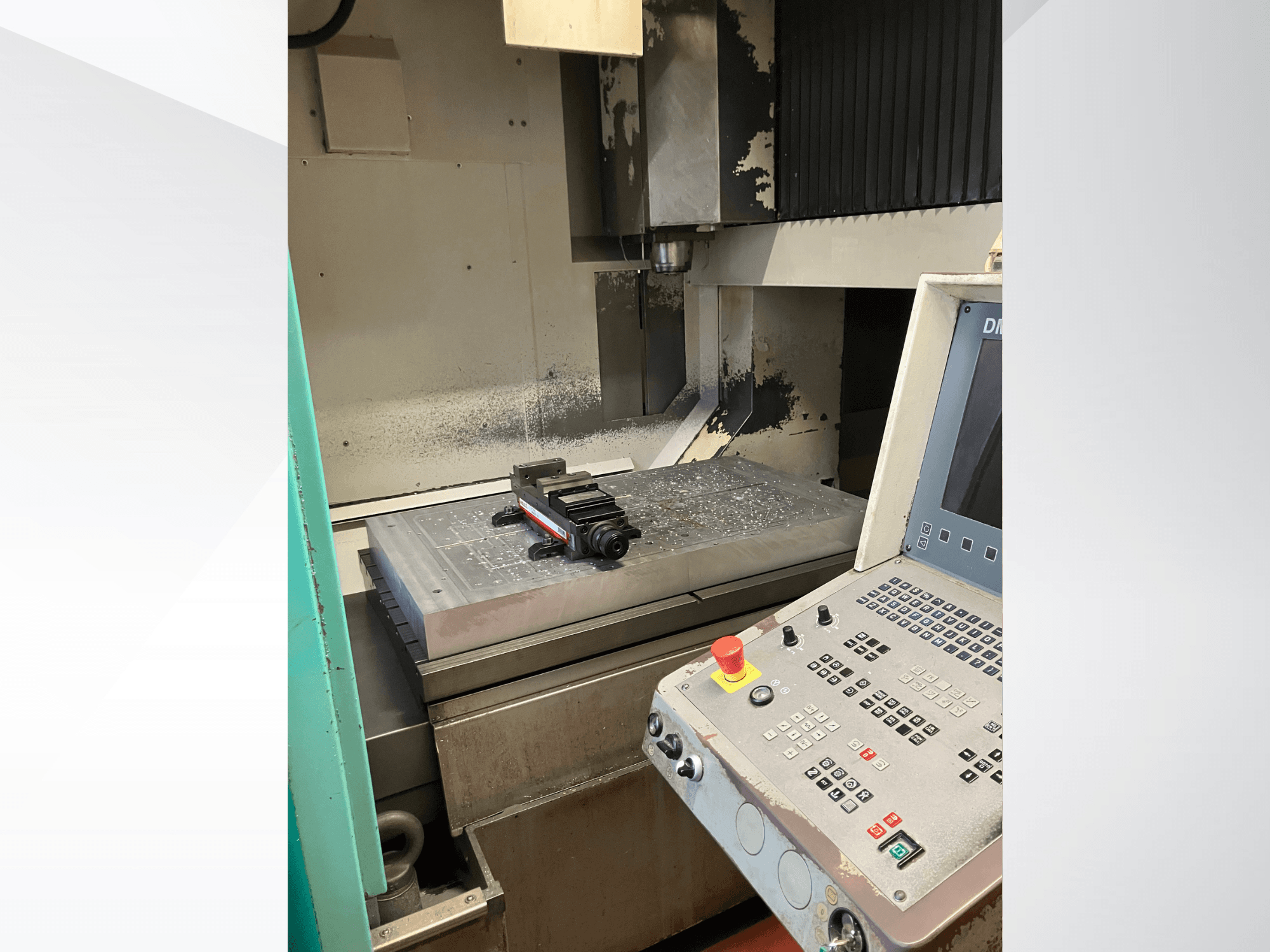Vertikālais apstrādes centrs DMG DMC 100 V hi-dyn, sānskats, kurā redzams vadības panelis un metāla detaļa uz galda.