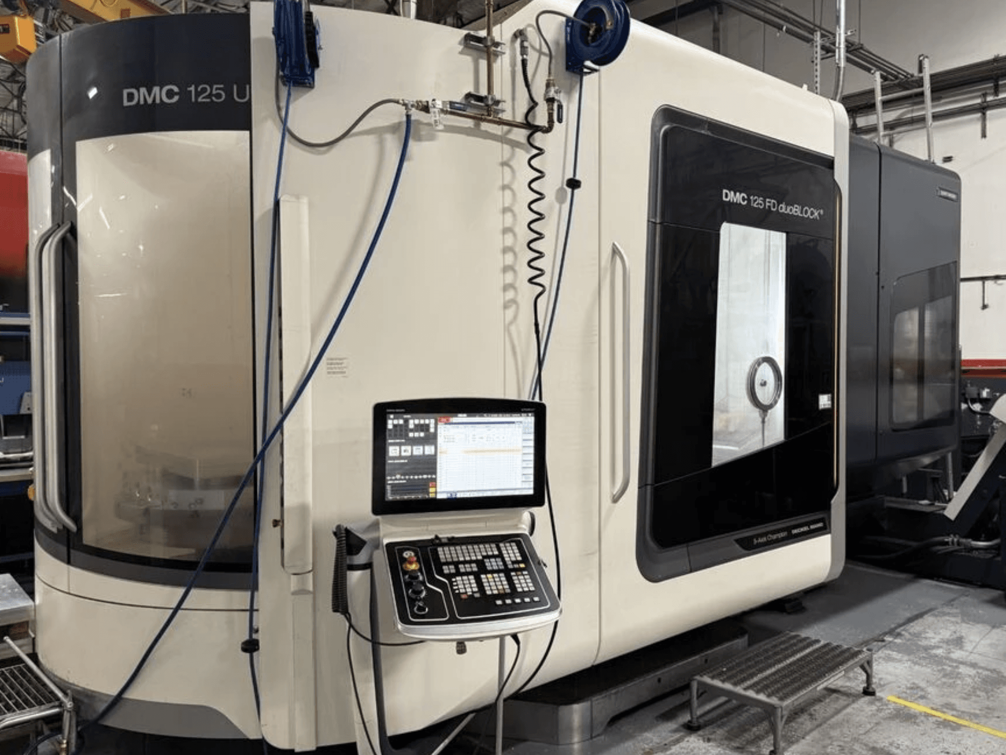 Universālais apstrādes centrs DMG MORI DMC 125 U duoBLOCK, skats no priekšpuses ar vadības paneli un atstarojošām virsmām.