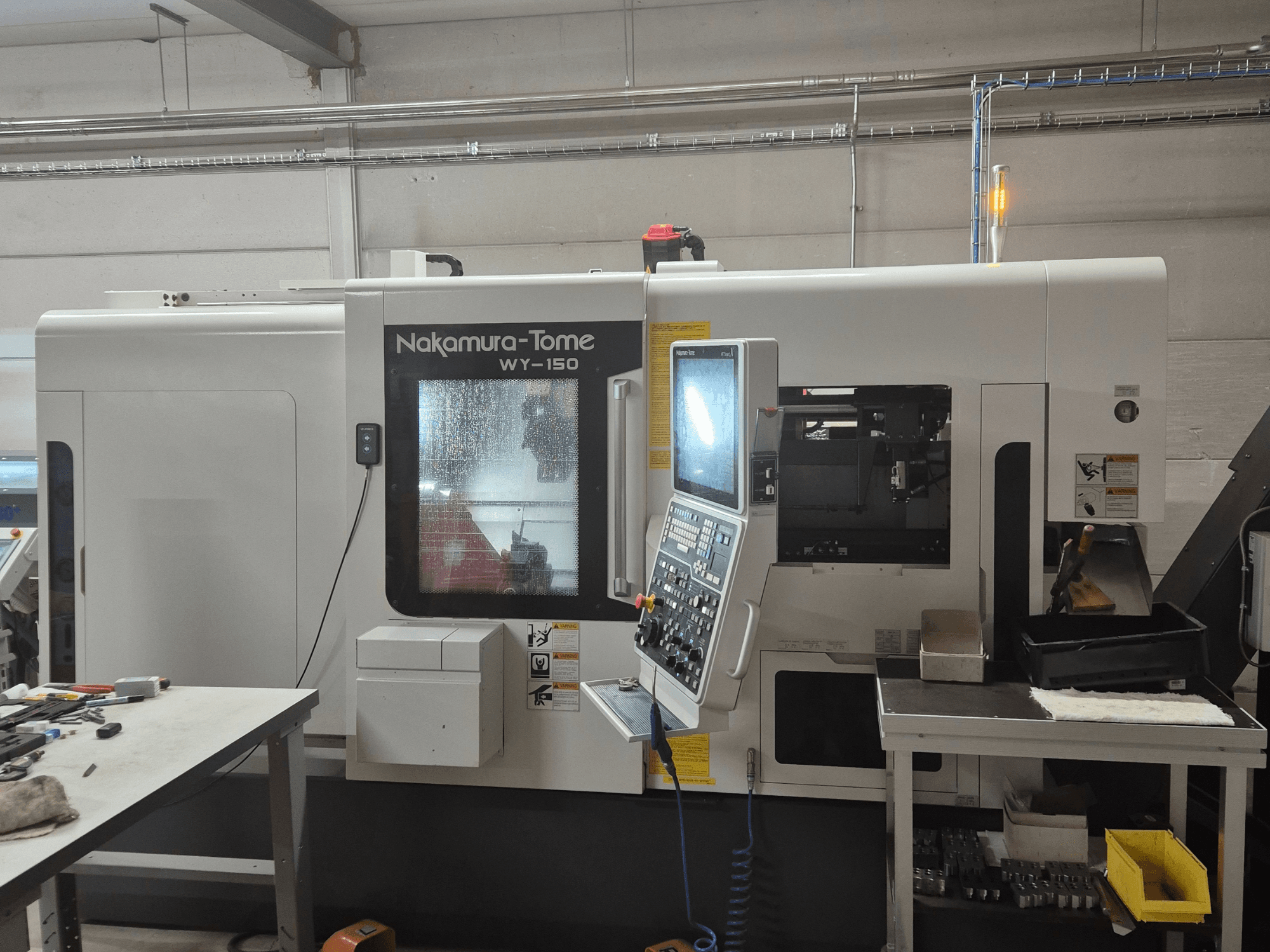 Nakamura-Tome WY-150 CNC virpa sānu skatā, ar vadības paneli, caurspīdīgu logu un redzamu darba zonu.