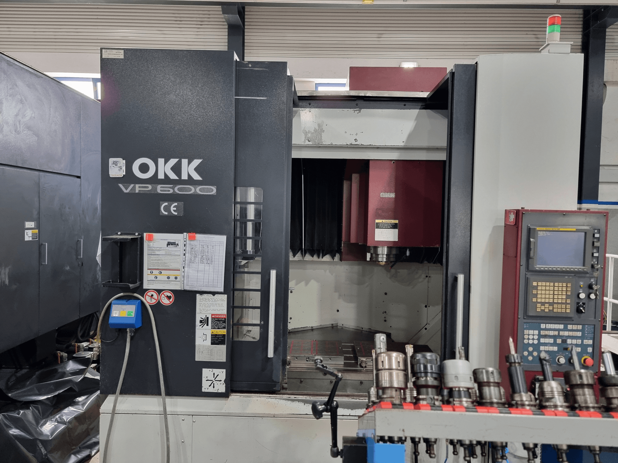 OKK VP600 vertikālais apstrādes centrs, skats no priekšpuses, kurā redzams vadības panelis un instrumentu turētāji uz statņa.