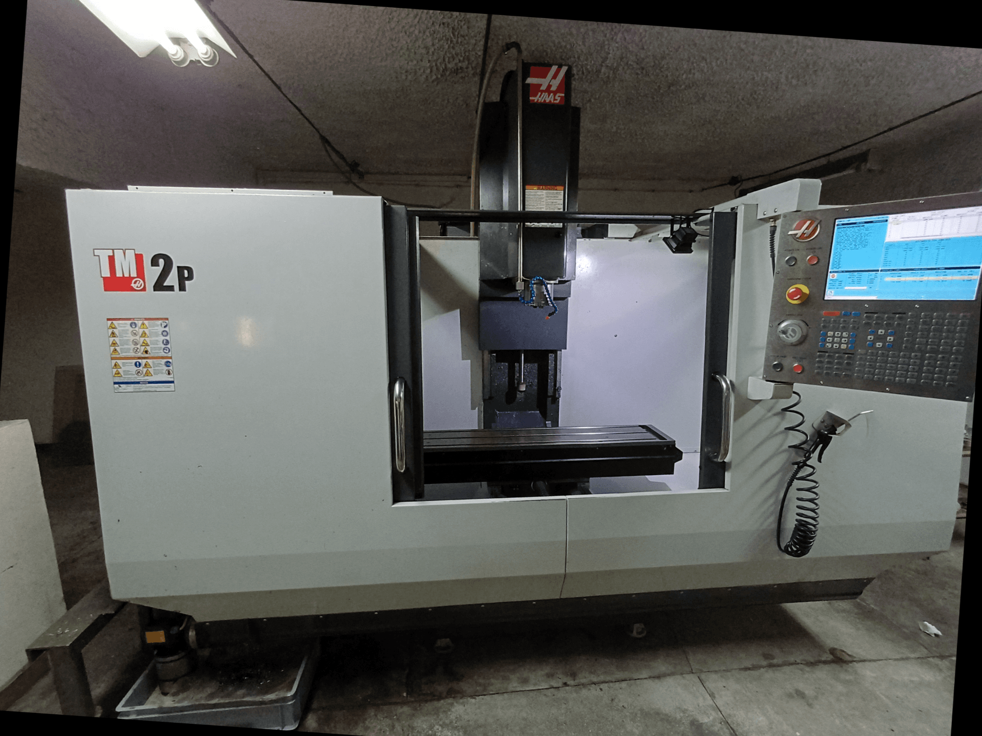HAAS TM-2P vertikālās apstrādes centrs, priekšējais skats, kurā redzams vadības panelis, vārpstas galva un darbgalds.