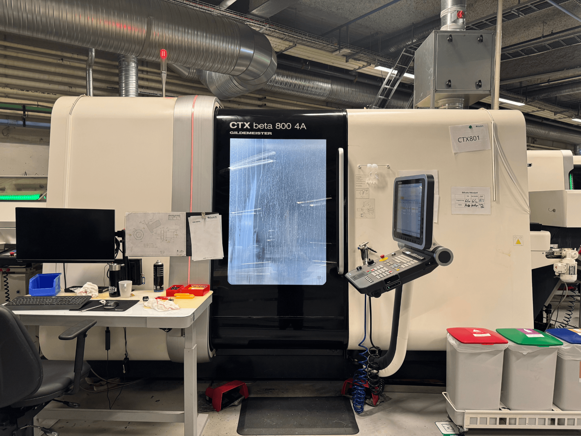 CTX beta 800 4A mašīna ar vadības paneli un monitoru, skats no sāniem, darbnīcā ar biroja iekārtojumu un krāsainiem atkritumu konteineriem.