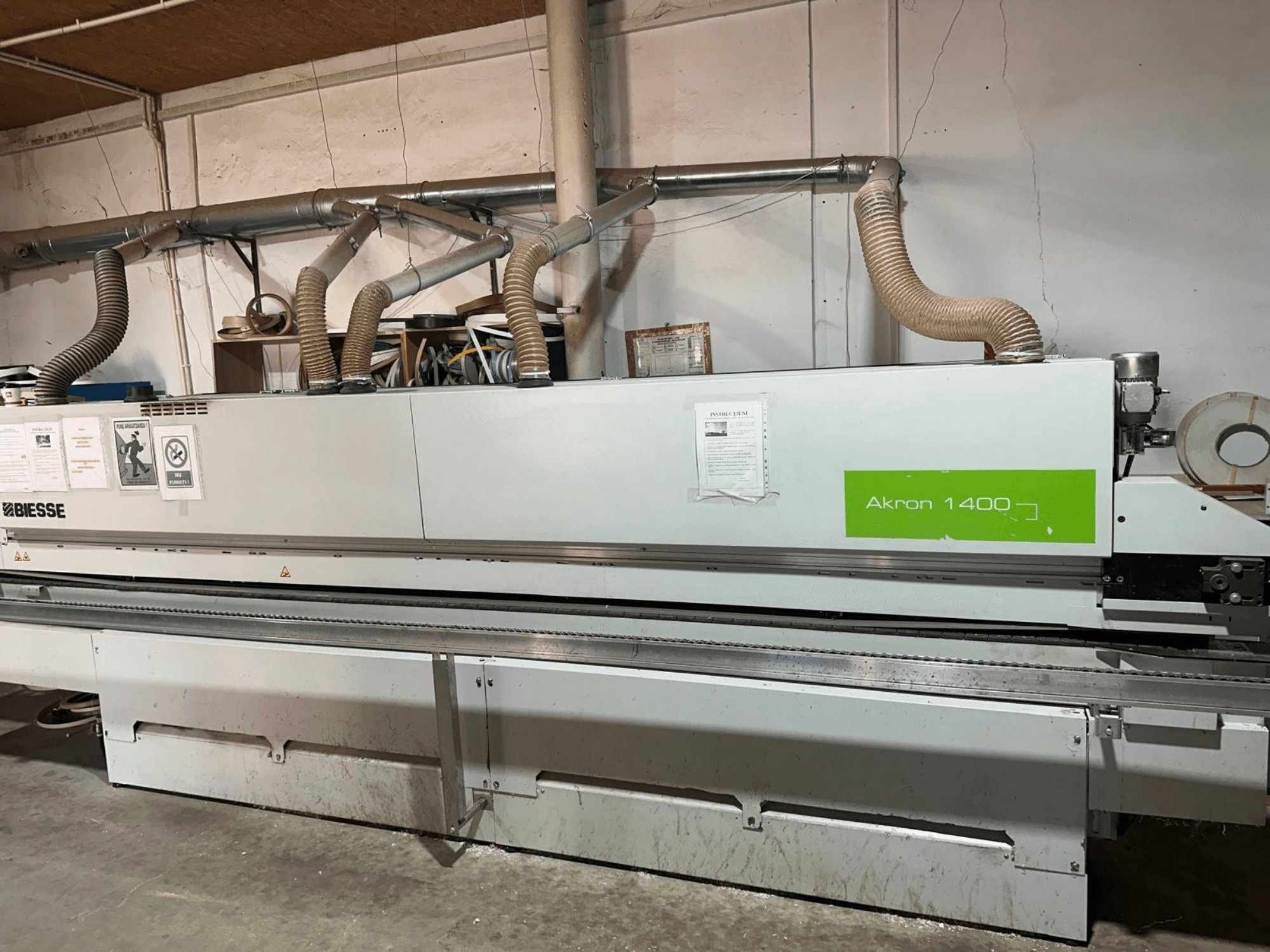 BIESSE Akron 1440 A malu līmēšanas mašīna no sāniem, kurā redzamas ventilācijas caurules, vadības panelis un ekspluatācijas uzlīmes.