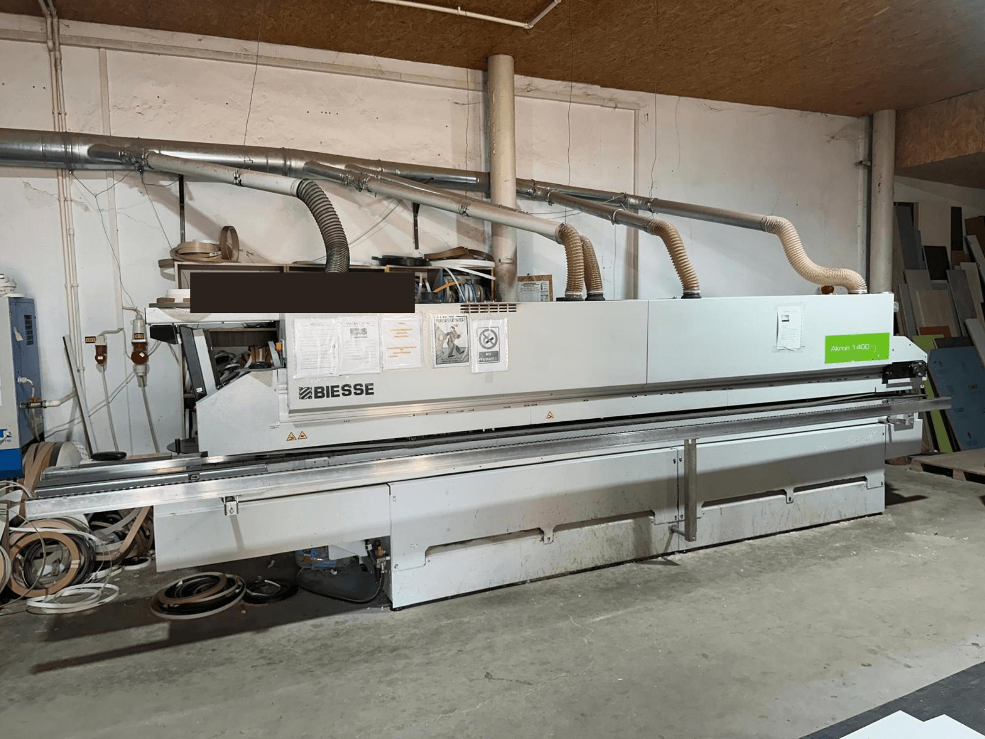 BIESSE AKRON 1440 A malu līmēšanas mašīna, skats no priekšpuses, kurā redzams vadības panelis un putekļu nosūces komponenti darbnīcas vidē.