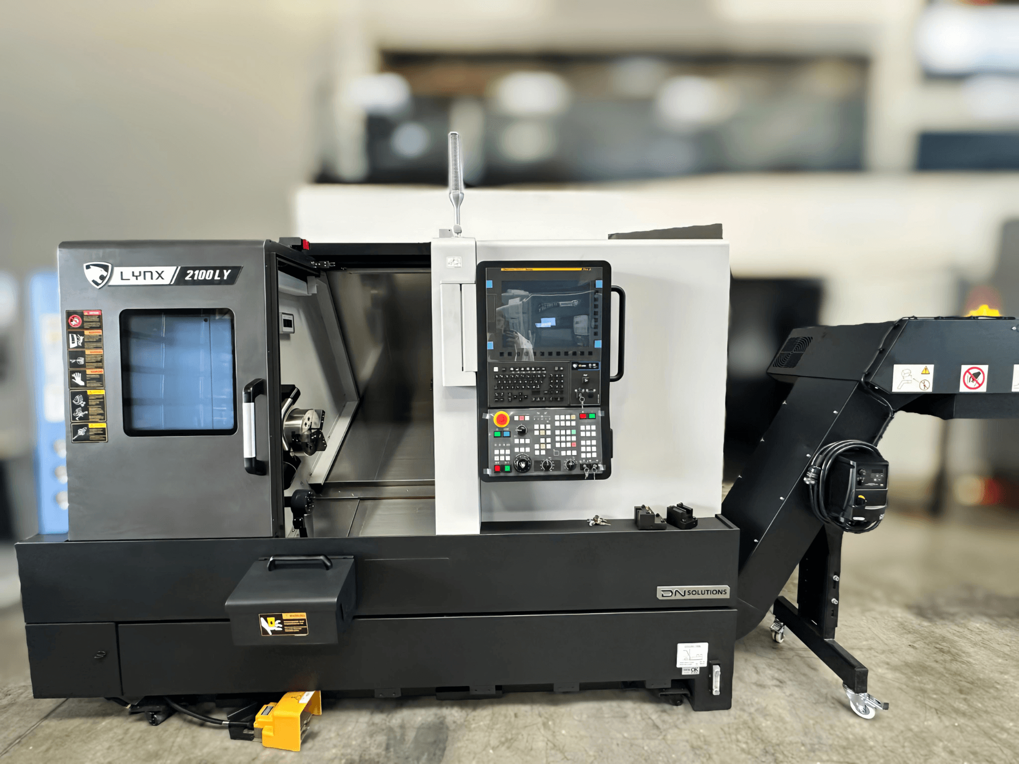 Horizontālās virpošanas iekārta DN SOLUTIONS LYNX 2100LYB, skats no priekšpuses, ar vadības paneli un atvērtām durvīm, kas atklāj iekšpusi.