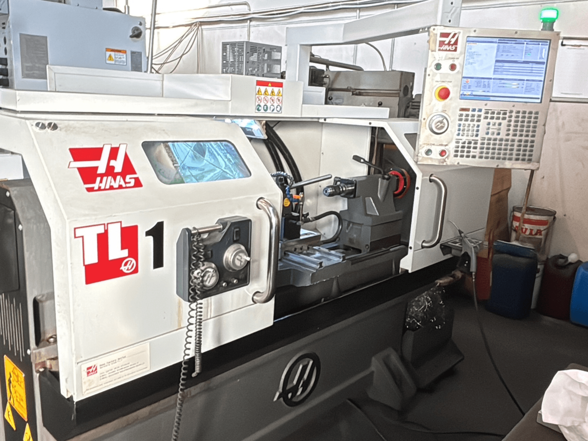 Haas TL-1 CNC virpmašīna, skats no priekšpuses, vadības panelis ar displeju, instrumentu turētājs un drošības uzlīmes.