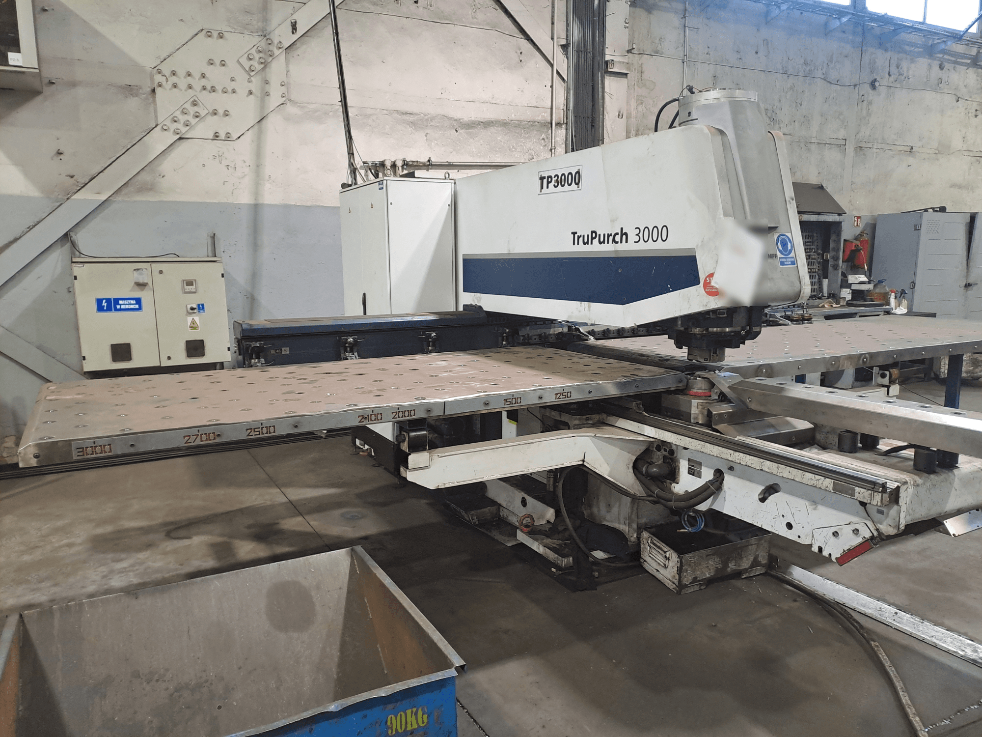 TruPunch 3000 CNC mašīna no priekšpuses ar lielu metāla plāksni un mērījumu marķējumiem rūpnieciskā vidē.