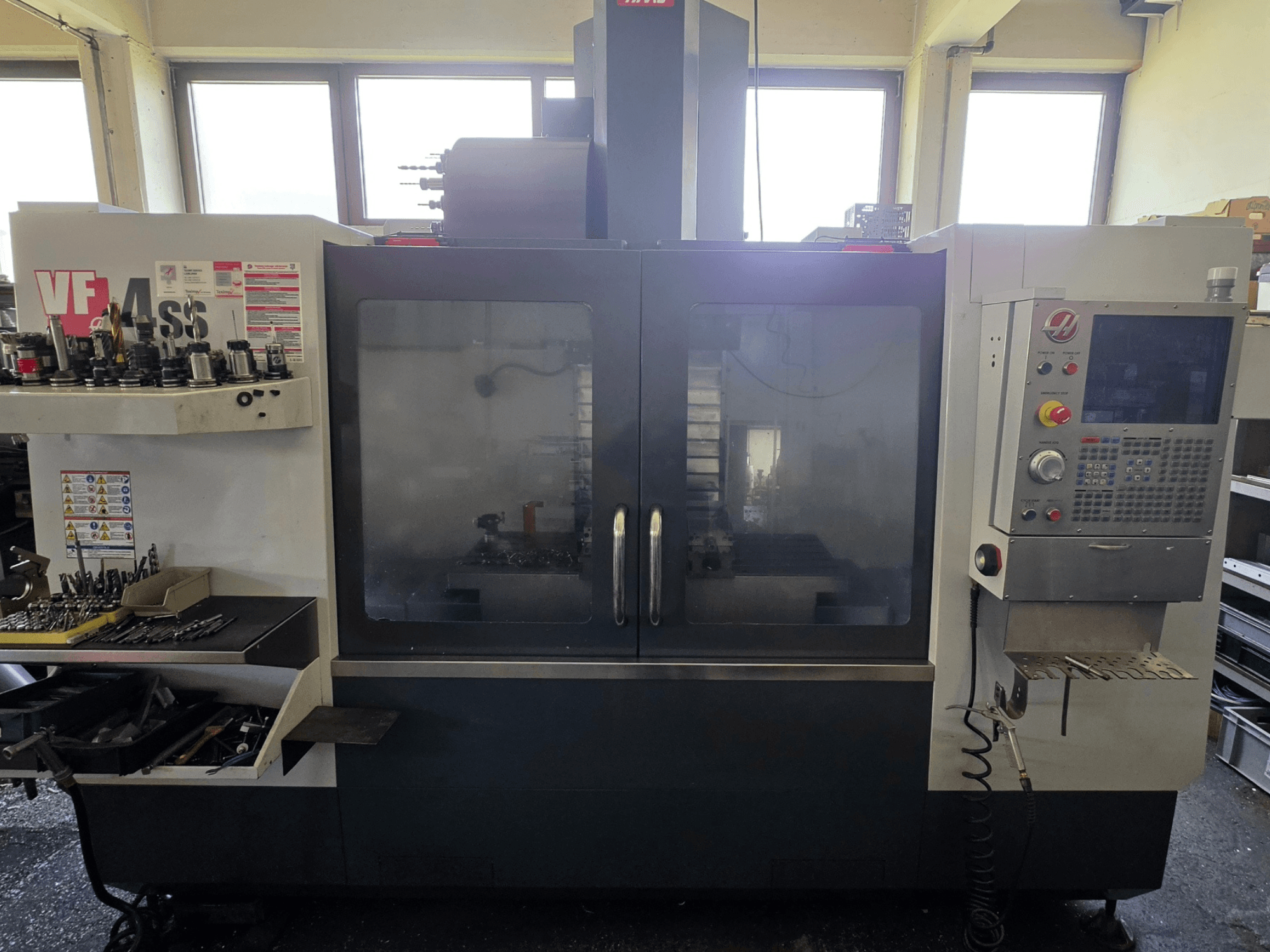 HAAS VF 34SS vertikālais apstrādes centrs no priekšpuses, kurā redzams vadības panelis un instrumentu glabāšanas zona.
