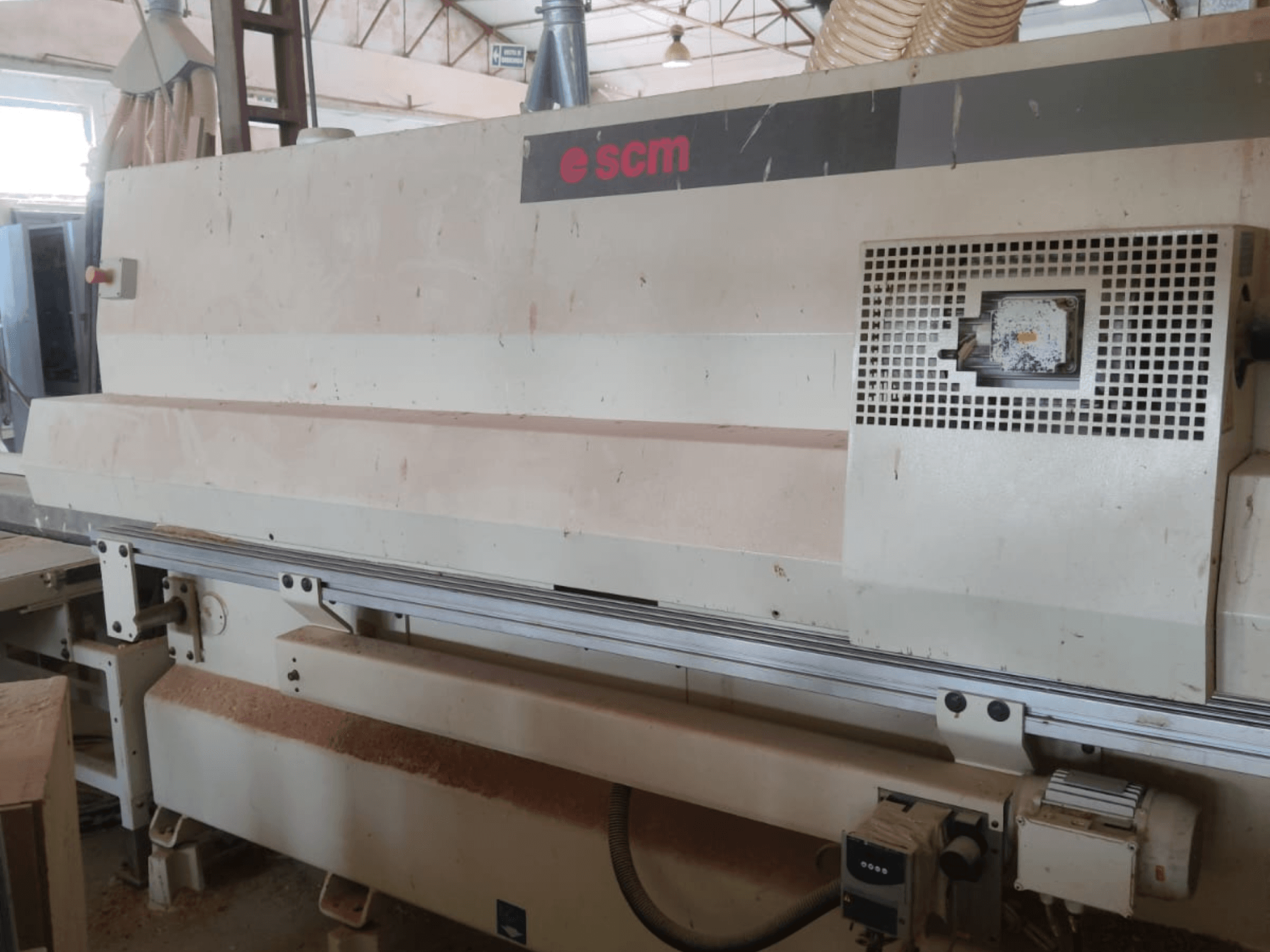 CNC koka apstrādes centrs SCM Windor60, skats no priekšpuses. Attēlā redzamas mašīnas vadības ierīces un putekļu savākšanas sistēma, zem kuras atrodas koka skaidas.