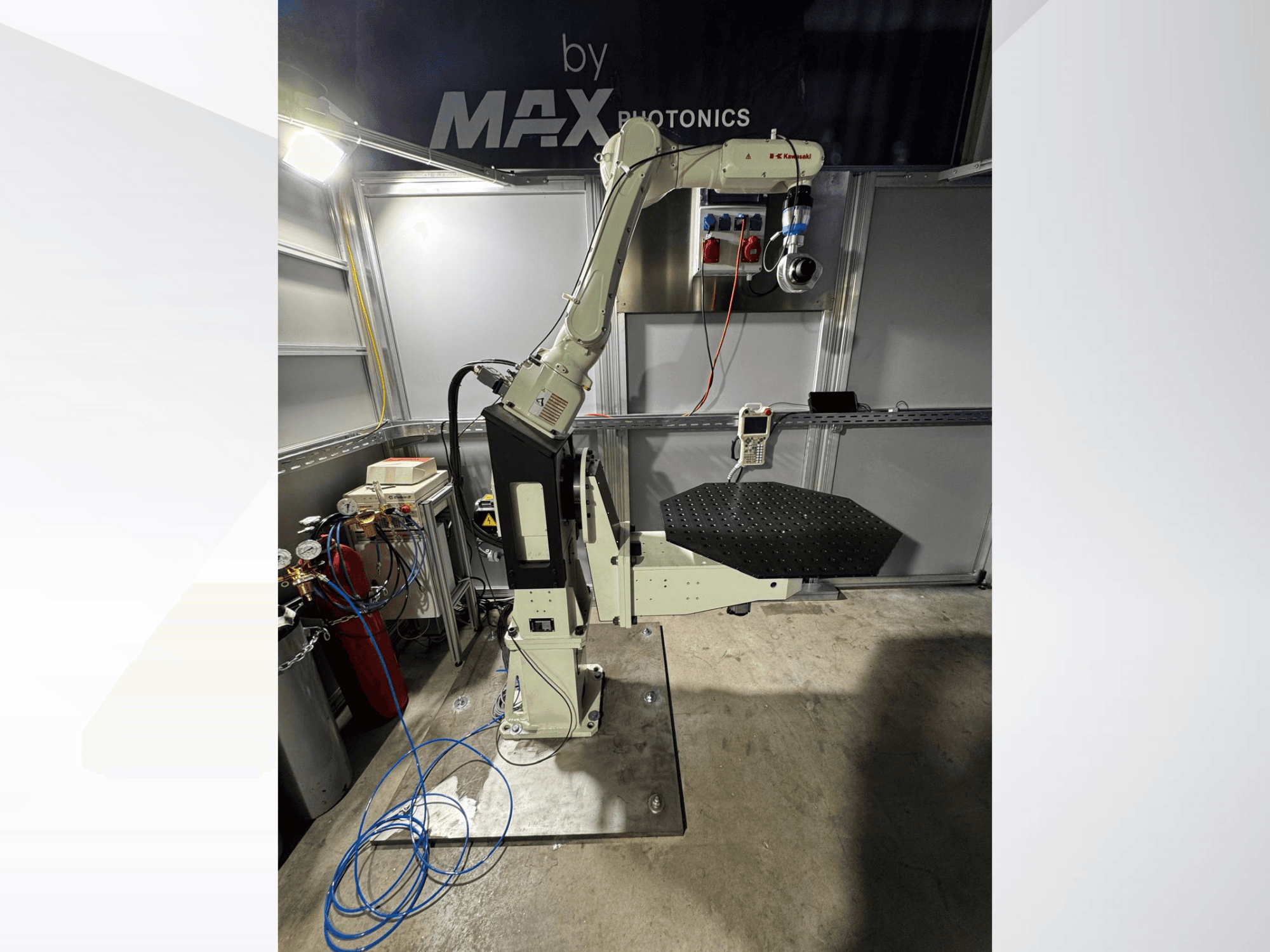 Max Photonics robotizētās rokas aparāts, skats no priekšpuses, ar melnu perforētu platformu un vadības paneli ar mērierīcēm un kabeļiem.