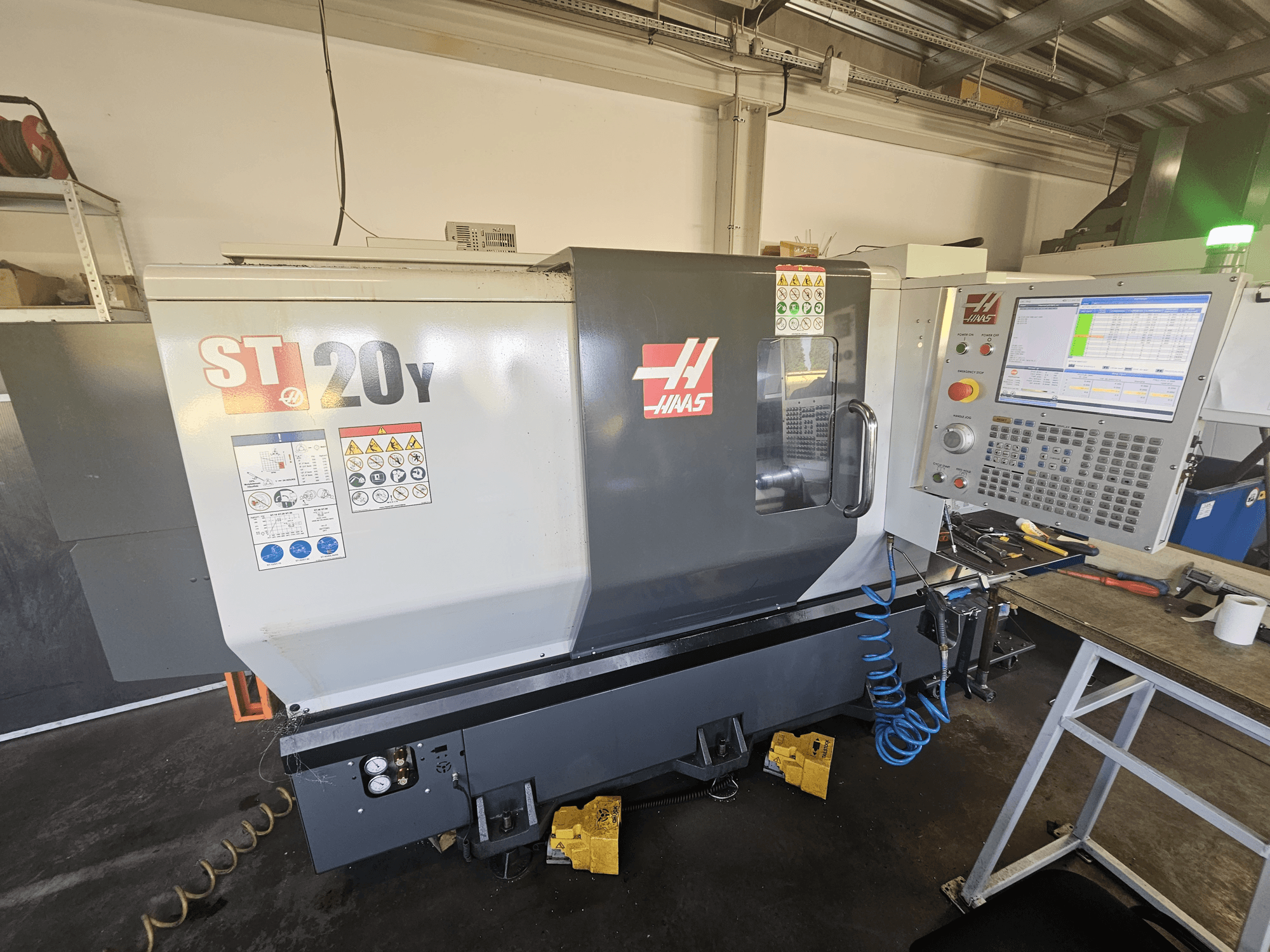 Haas ST-20Y CNC virpa priekšpusē ar vadības paneli; ietver drošības uzlīmes un gaisa šļūtenes detaļas sānos.