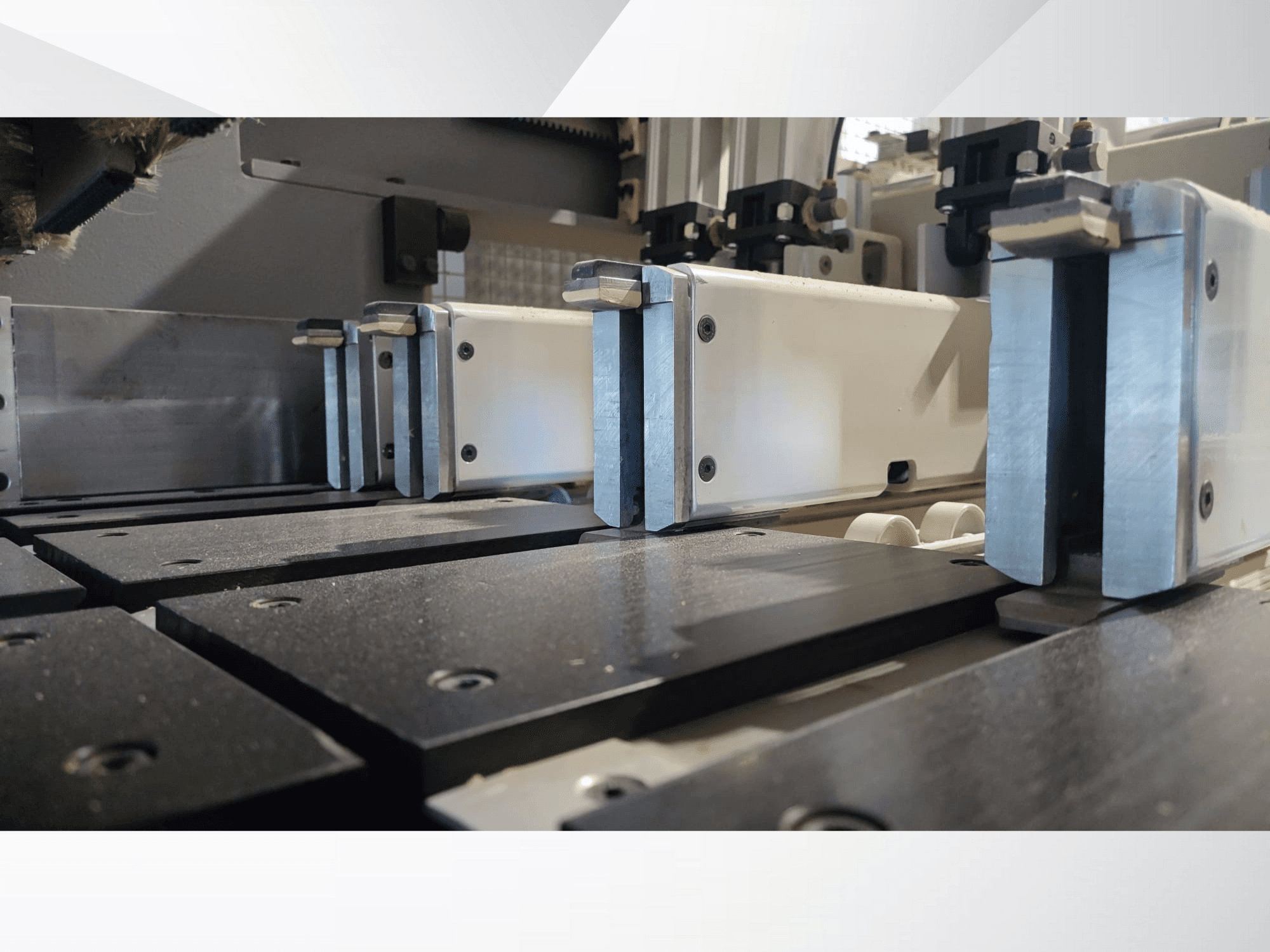 Precizitātes mašīnas fiksēšanas mehānisma ar metāla spailēm tuvplāna skats ar melnām darba virsmām un redzamām vadotnēm.