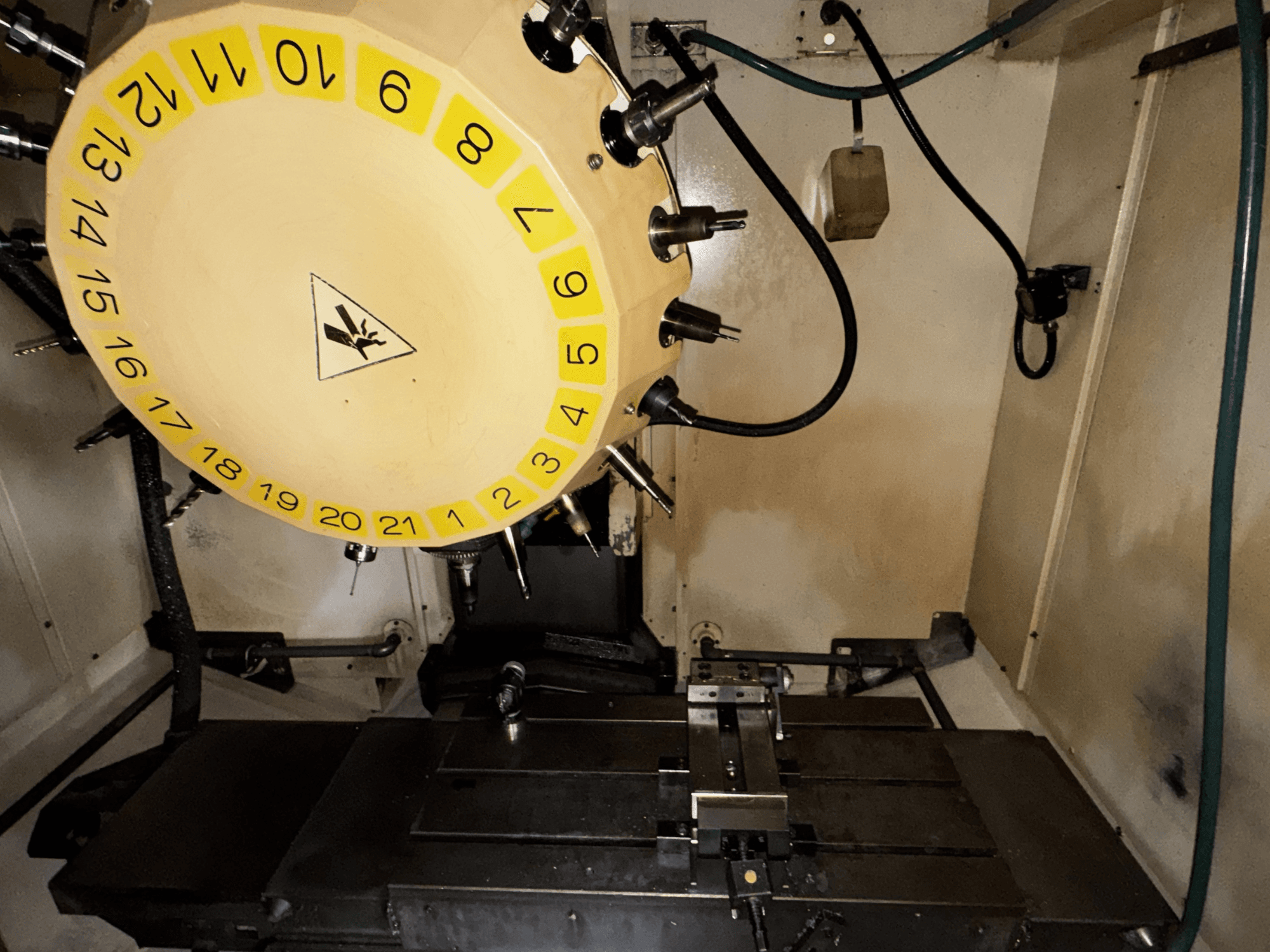 FANUC Robodrill alpha-T21iFL vertikālā apstrādes centra iekšējais skats ar redzamu instrumentu karuseli un apstrādes galdu.