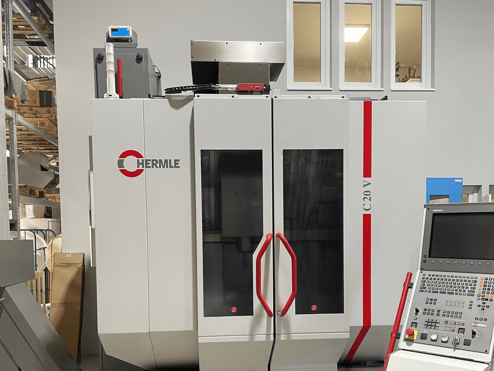 Chermle C20 V CNC mašīna, skats no priekšpuses, ar vadības paneli un sarkaniem rokturiem; industriāls dizains ar lielām stikla durvīm.